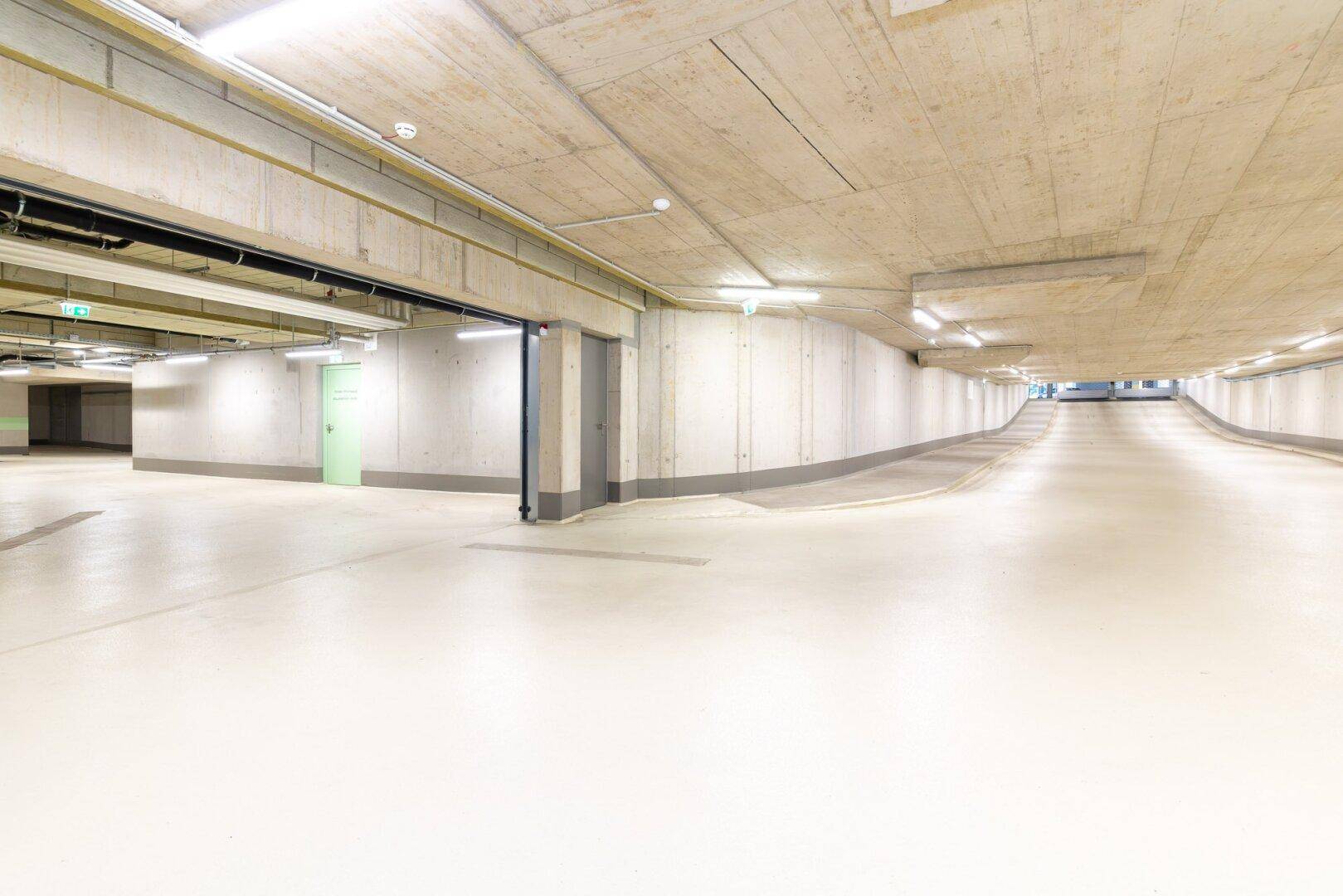 Weitläufige Tiefgarage mit hellen Wänden, glänzendem Boden und klarer Beleuchtung.