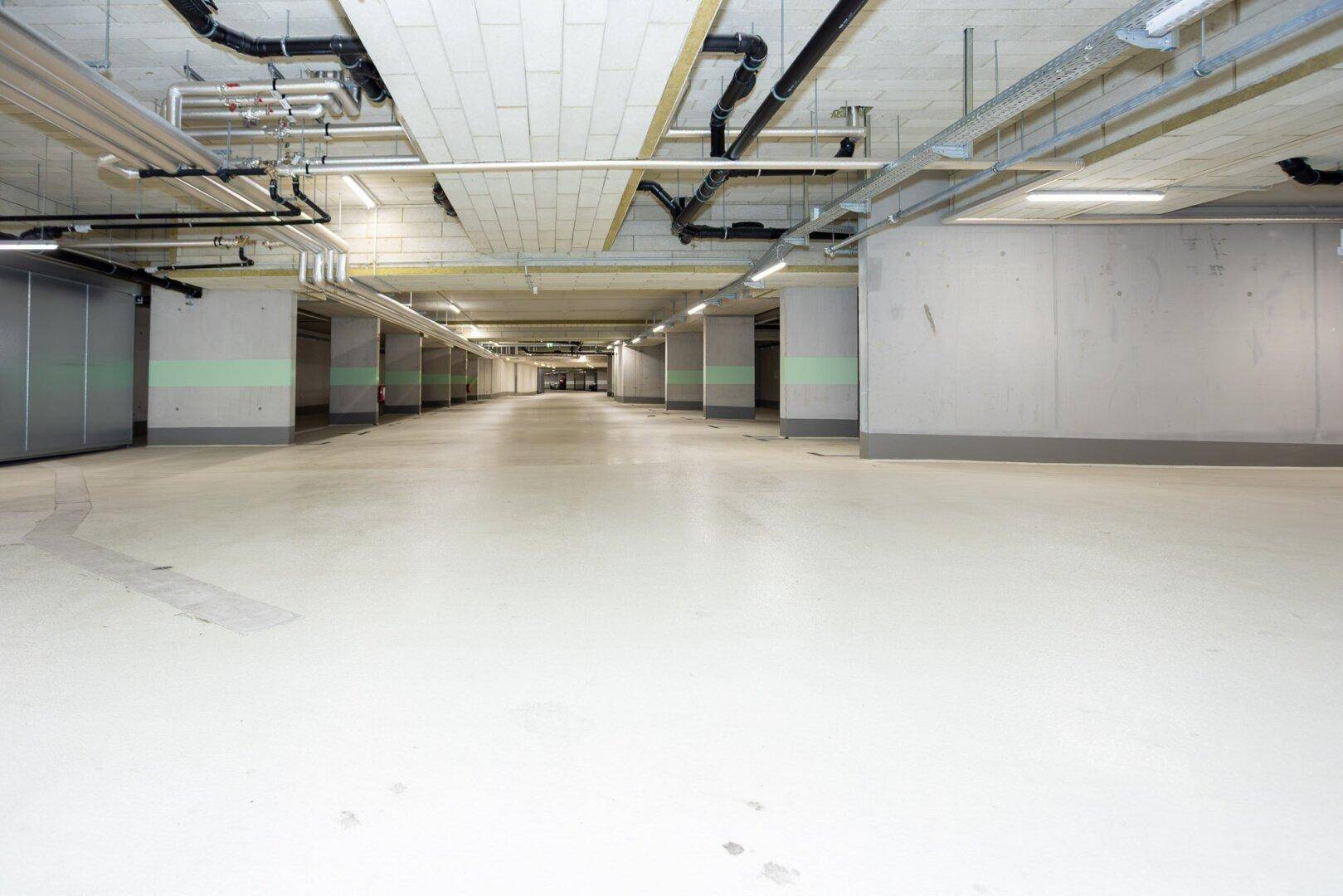 Lange, helle Tiefgarage mit Betonpfeilern und glattem Boden, bereit für Fahrzeuge.