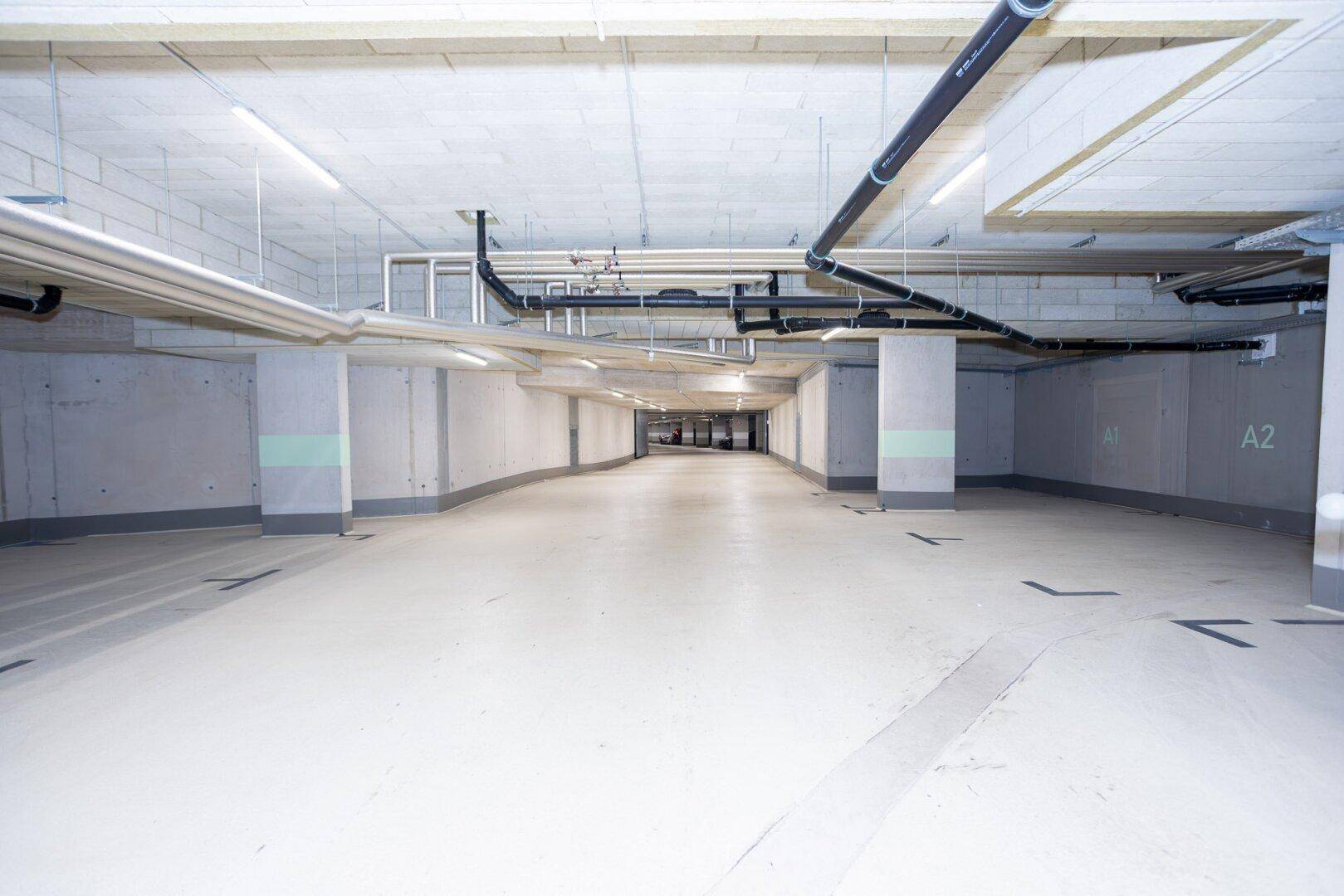 Geräumige Tiefgarage mit Betonstützen, sichtbaren Leitungen und heller, funktionaler Beleuchtung.