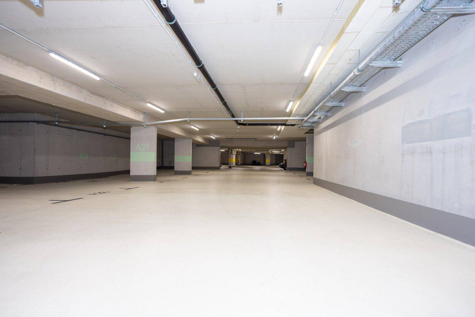 Saubere und gut beleuchtete Tiefgarage mit markierten Stellplätzen und Betonwänden.