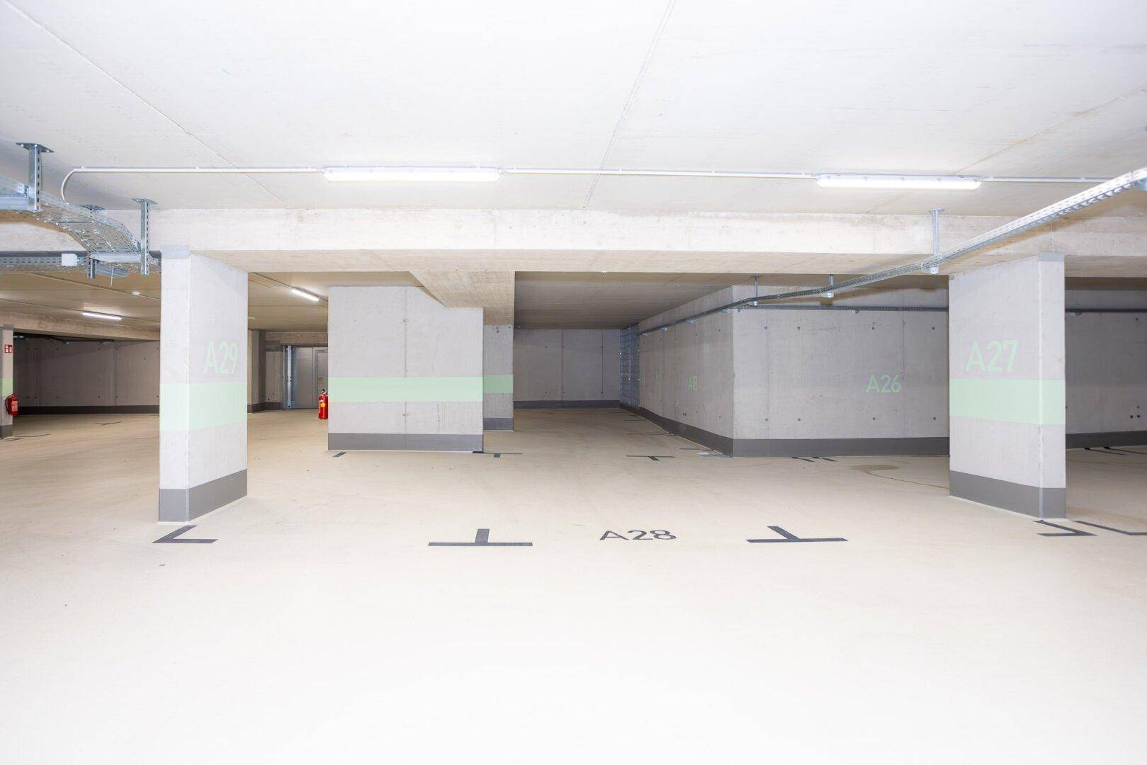 Helle Tiefgarage mit Betonstützen, glattem Boden und klarer Beschilderung für die Parkplätze.