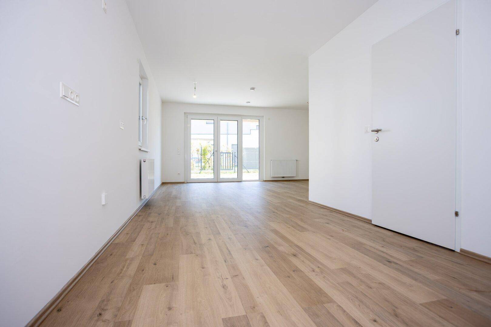 Geräumiger, unmöblierter Wohnbereich mit hellem Laminatboden und großen Fenstern für viel Tageslicht.