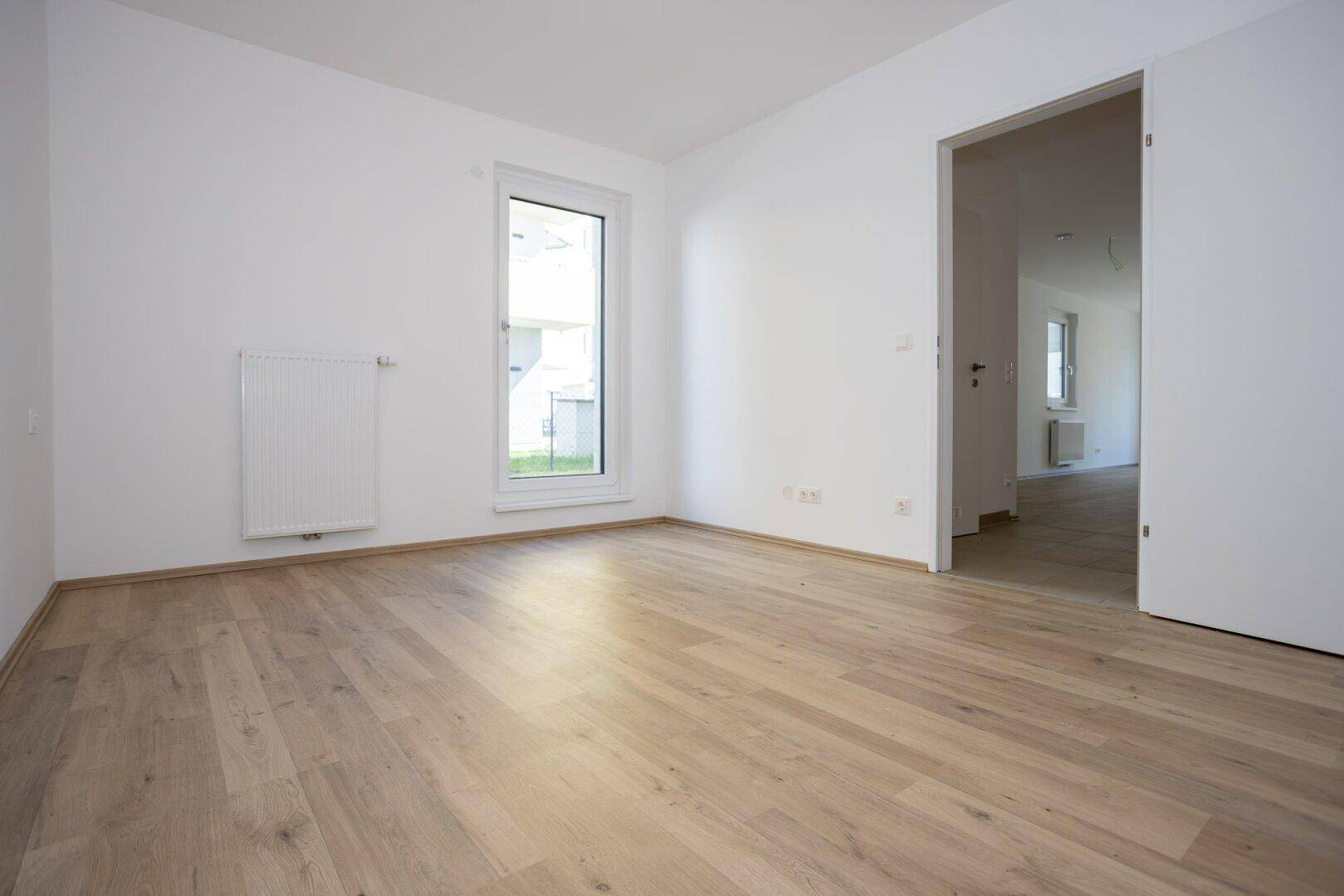 Geräumiges Schlafzimmer mit hellem Laminatboden, weiß gestrichenen Wänden und Zugang zu weiteren Räumen.