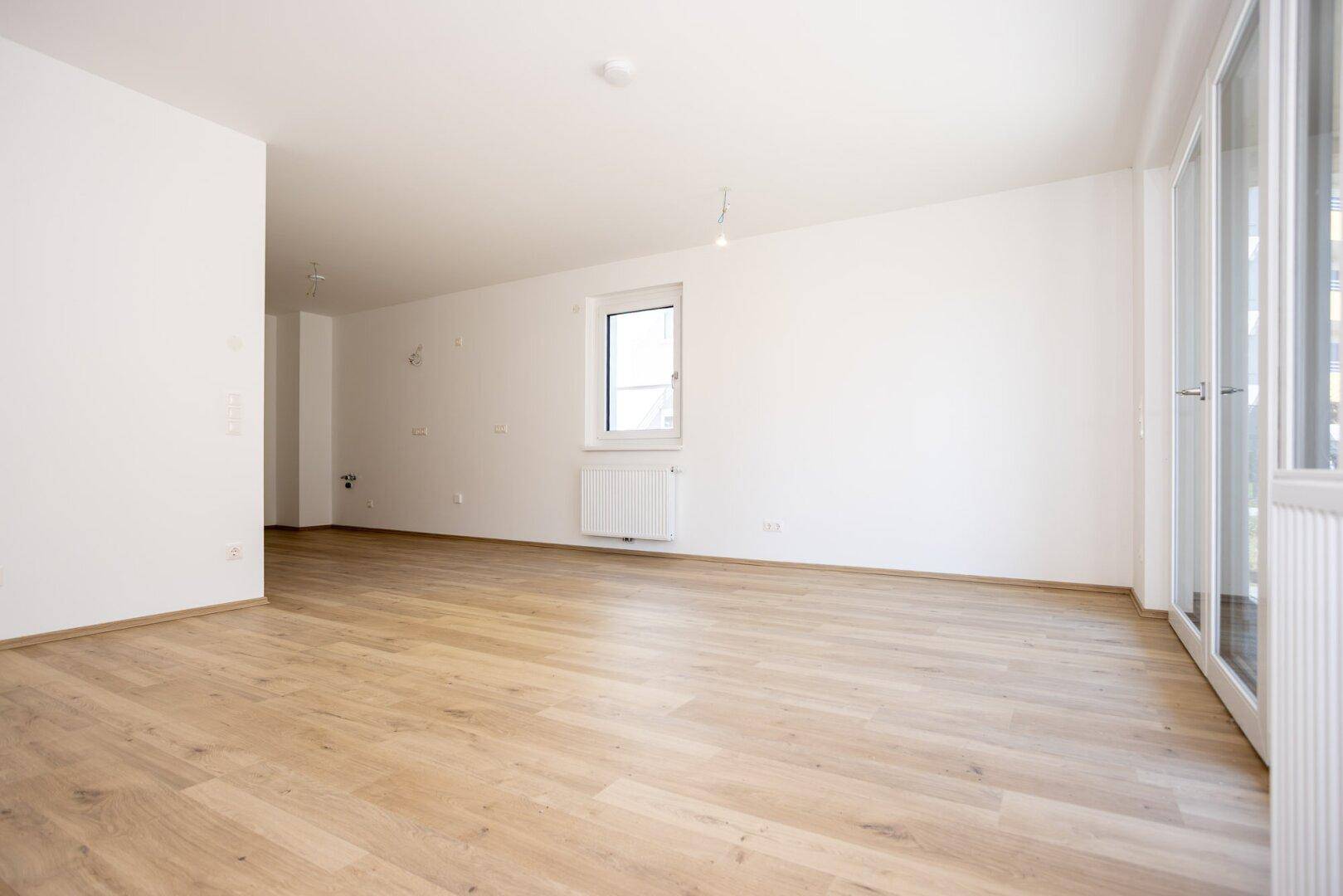 Lichtdurchfluteter Wohnraum mit hellem Laminatboden, weiß gestrichenen Wänden und Heizkörper.