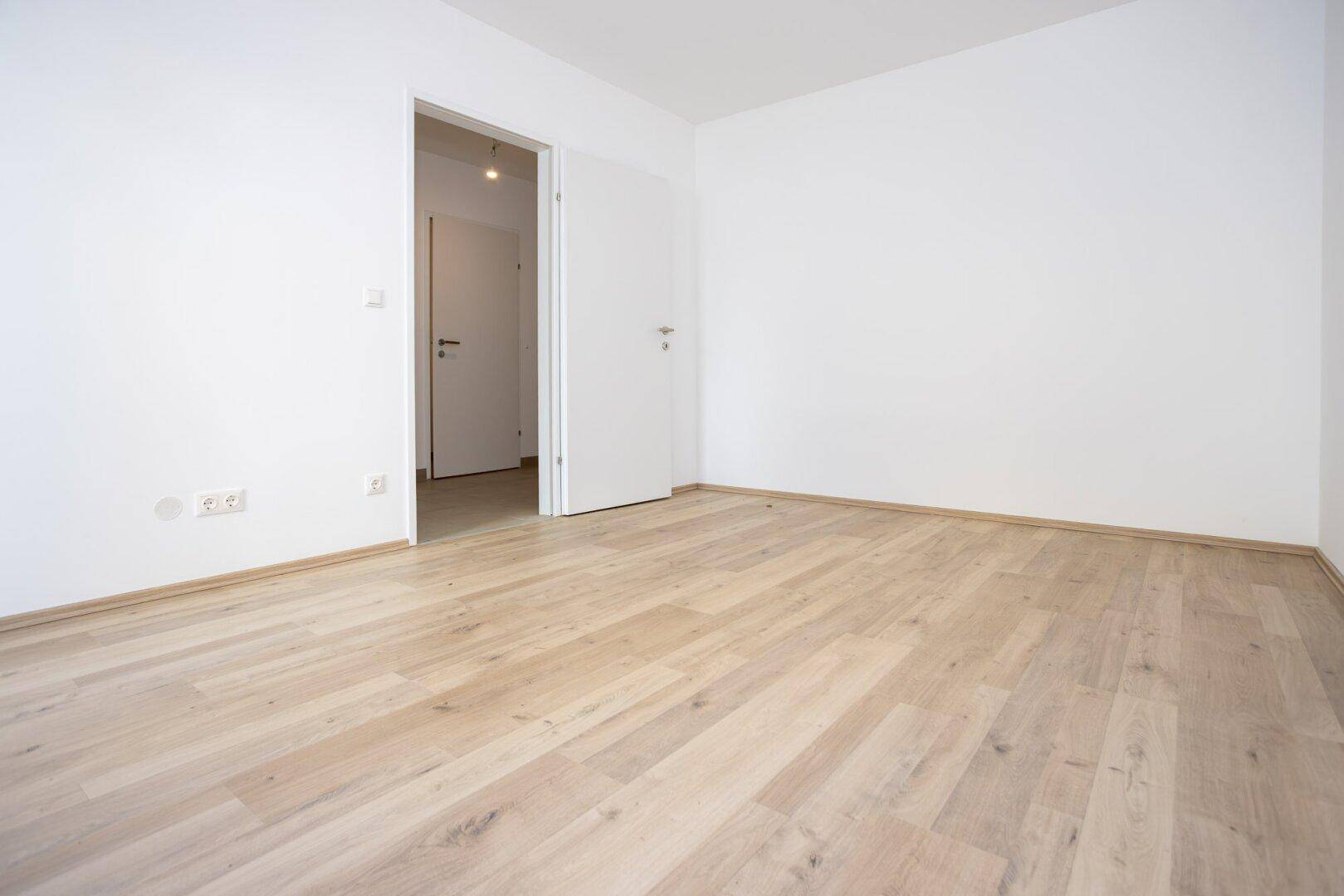Unmöbliertes Zimmer mit hellem Laminatboden und weiß gestrichenen Wänden, bereit zum Einzug.