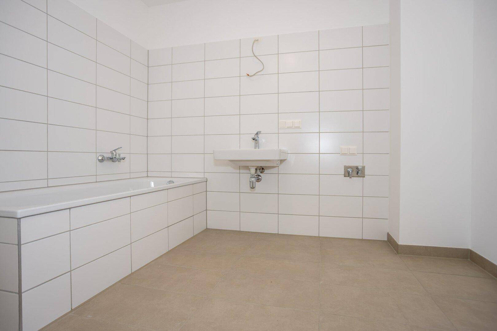 Modernes Badezimmer mit weißen Wandfliesen, beigen Bodenfliesen, Badewanne und Waschbecken.