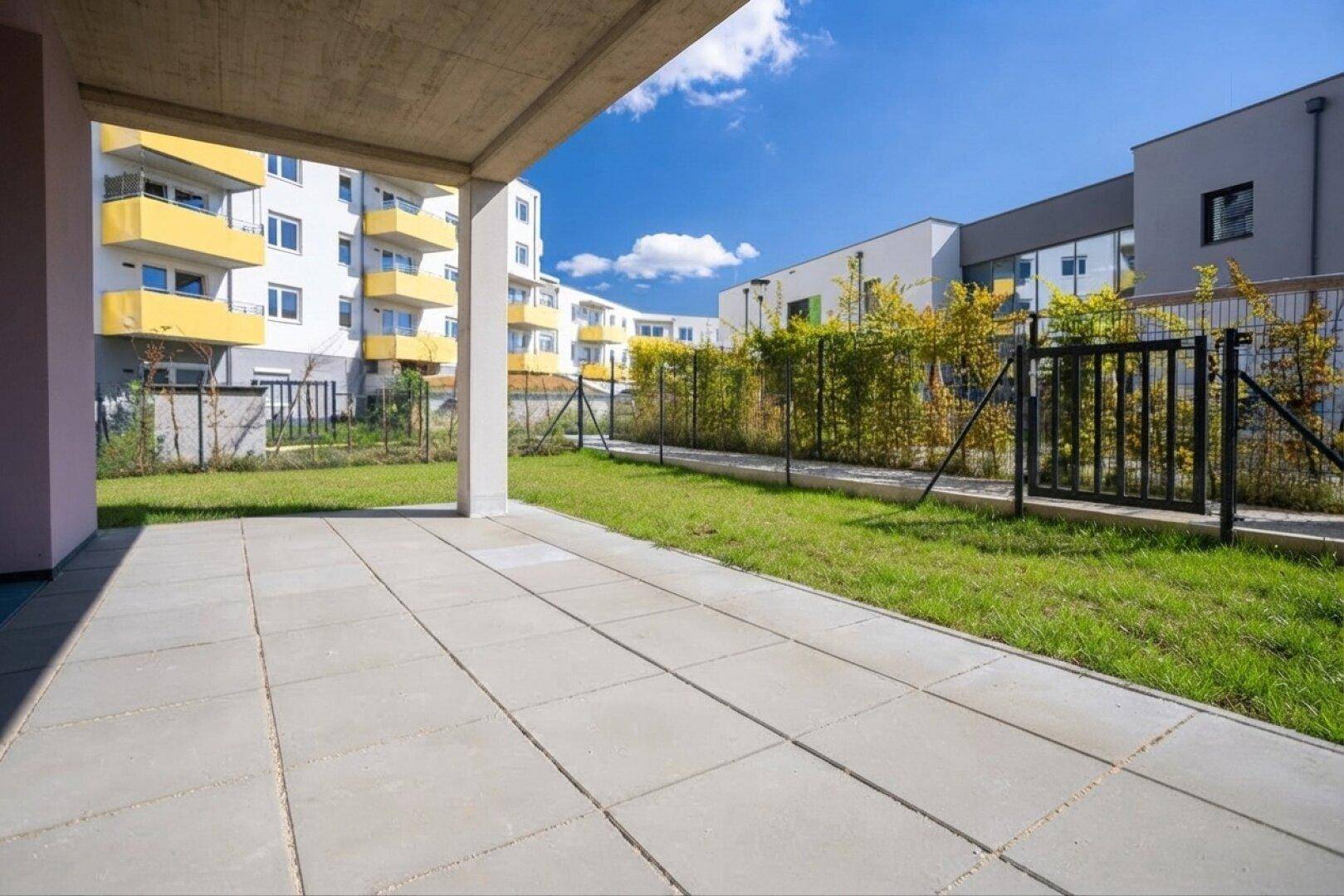 Geräumige Terrasse mit Rasen und Blick auf die umliegenden Neubauten mit gelben Balkonen.