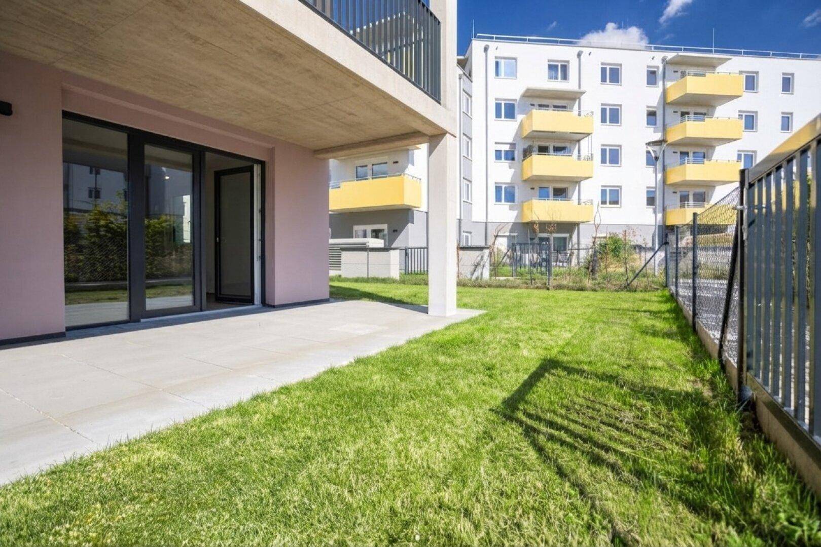 Sonniger Terrassenbereich mit direktem Zugang zum Garten und Blick auf die moderne Wohnanlage.