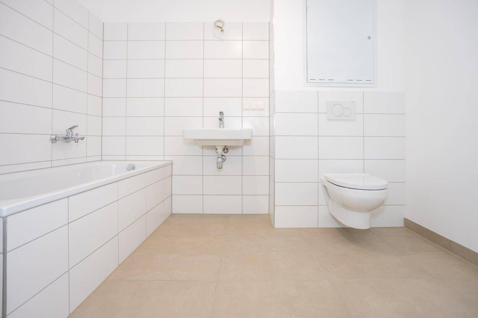 Modernes Badezimmer mit weißen Fliesen, Badewanne, Waschbecken und wandhängendem WC.