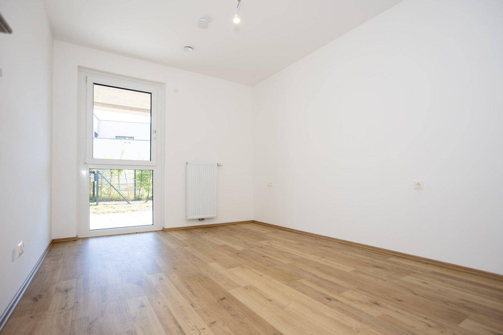 Helles Schlafzimmer mit Holzboden, weiß gestrichenen Wänden und einem großen Fenster.