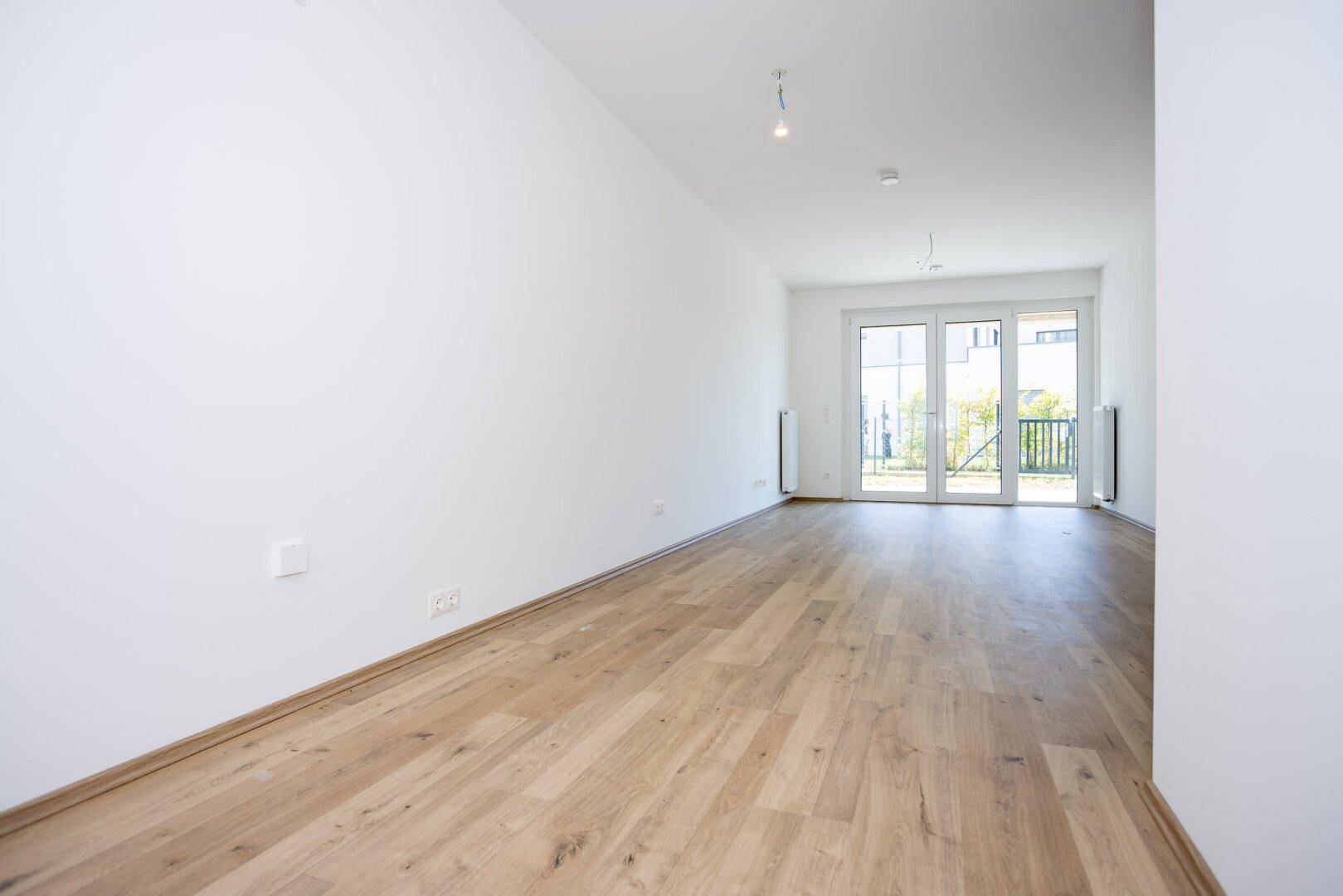 Geräumiges, leeres Wohnzimmer mit Parkettboden und Zugang zu einem Balkon oder einer Terrasse.