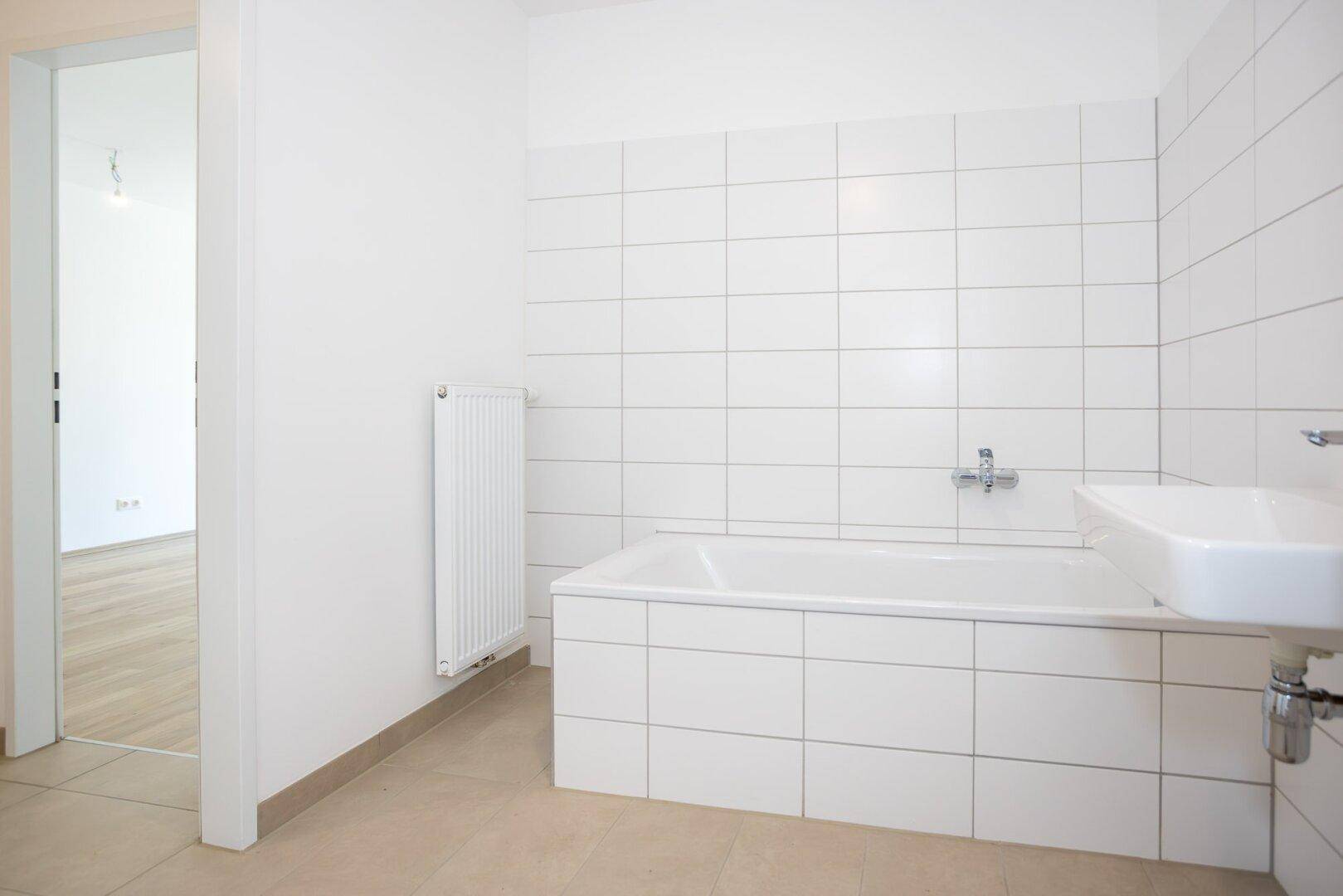 Badezimmer mit Badewanne, Waschbecken und Heizkörper, bereit für die Endmontage.