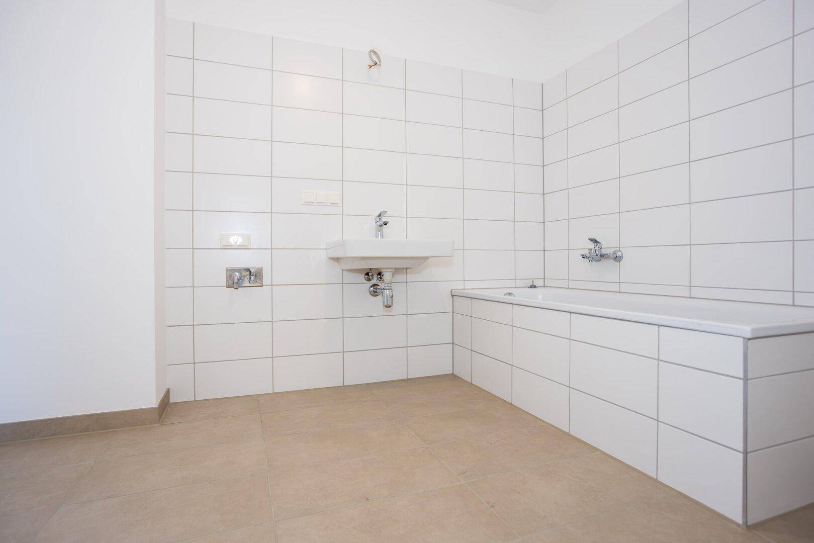 Modernes Badezimmer mit weißen Wandfliesen, Waschbecken und integrierter Badewanne.