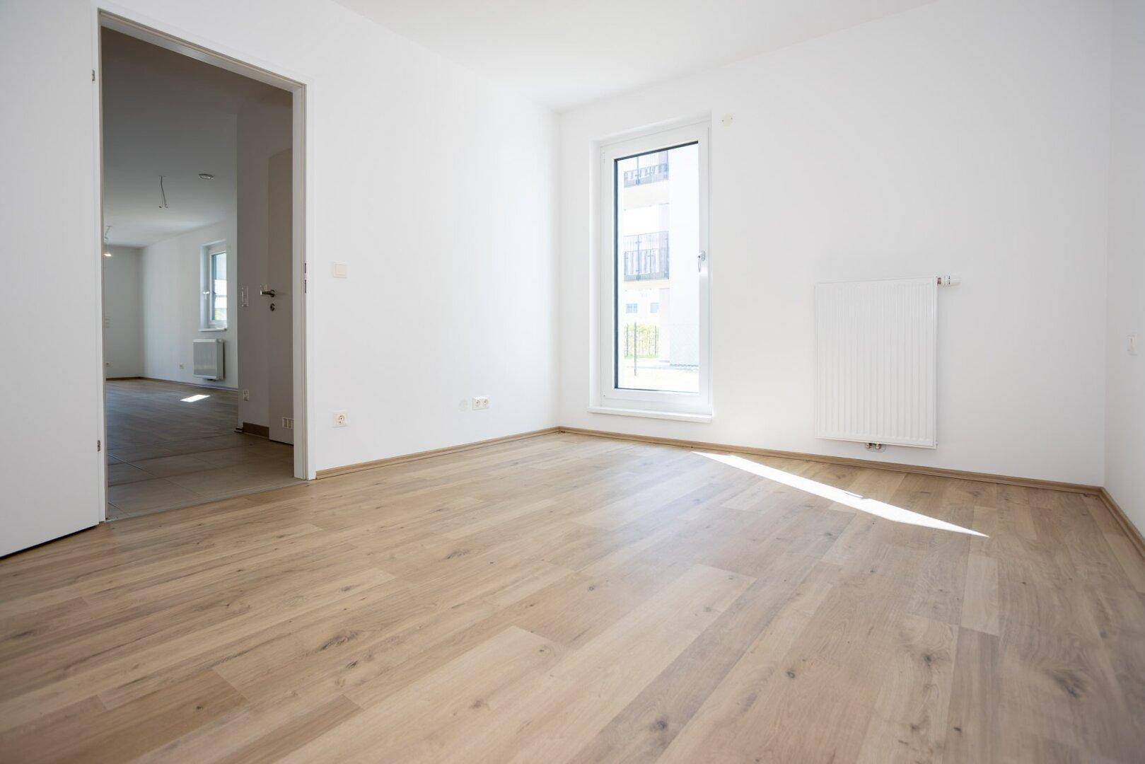 Helles Schlafzimmer mit Laminatboden und großem Fenster, bereit zur individuellen Gestaltung.