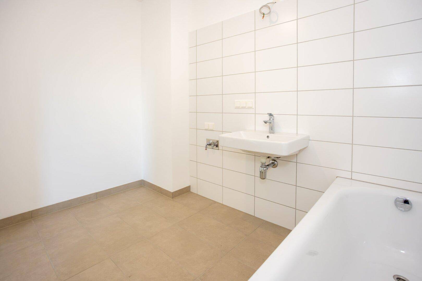 Helles Badezimmer mit weiß gefliesten Wänden, Waschbecken und Badewanne.