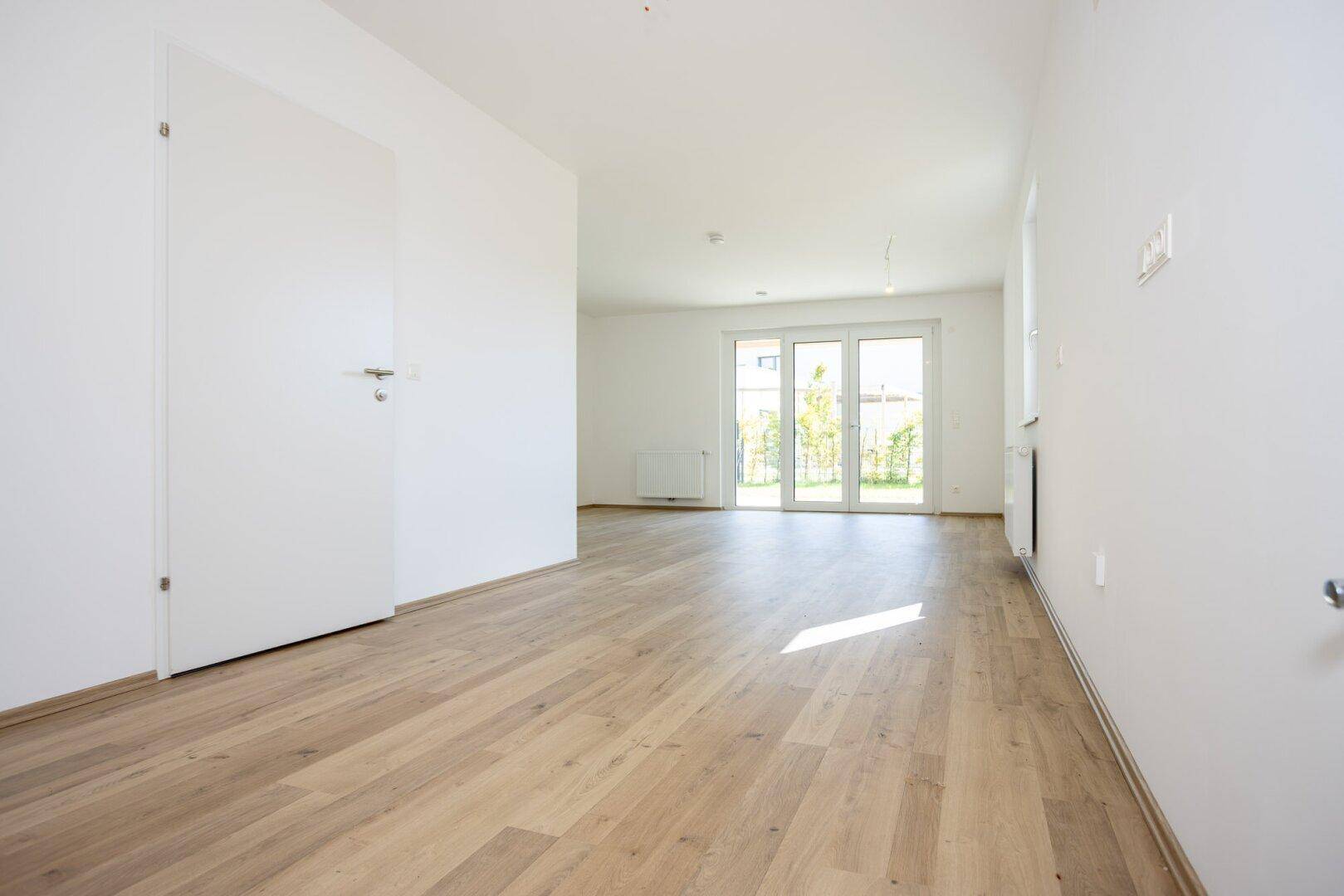 Lichtdurchfluteter Wohnbereich mit hellem Laminatboden und direktem Zugang zur Terrasse.