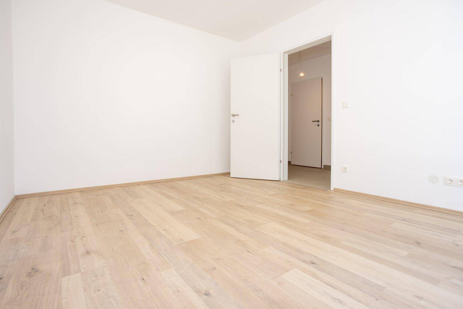 Unmöbliertes Schlafzimmer mit hellem Laminatboden und Zugang zu weiteren Räumen.