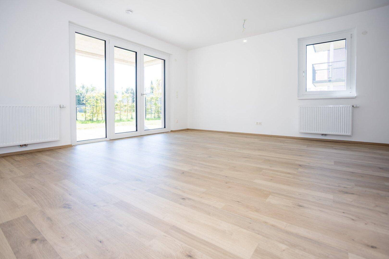 Große Fenstertüren und Fenster sorgen für viel Tageslicht im geräumigen Wohnzimmer.