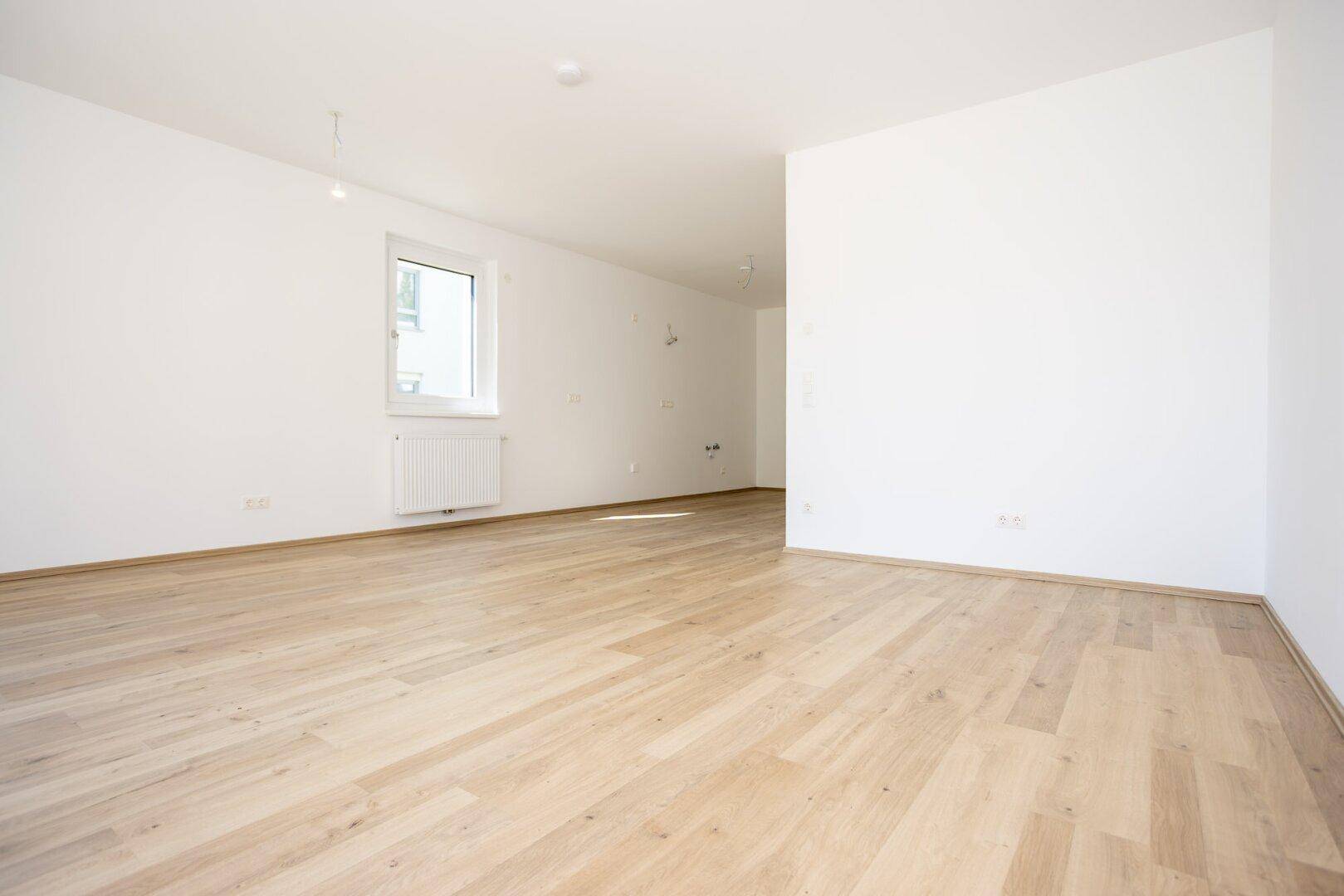 Geräumiger, unmöblierter Wohnbereich mit hellem Laminatboden und weißen Wänden.