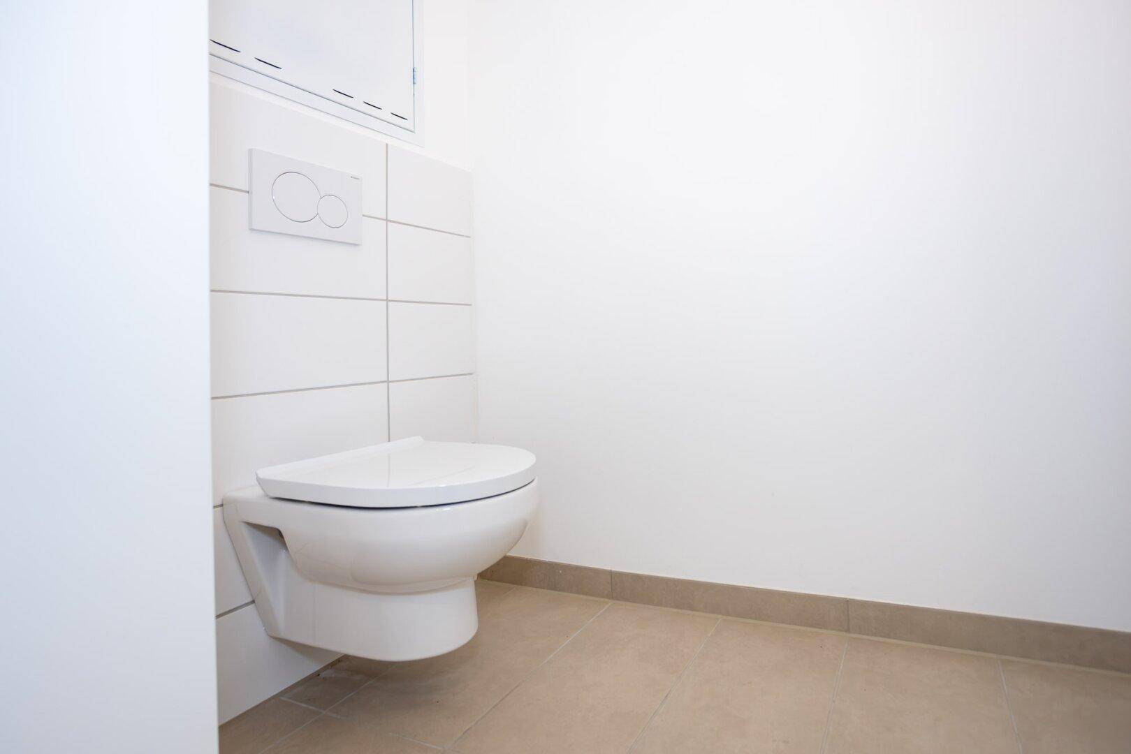 Separates WC mit wandhängender Toilette und modernen weißen Fliesen.