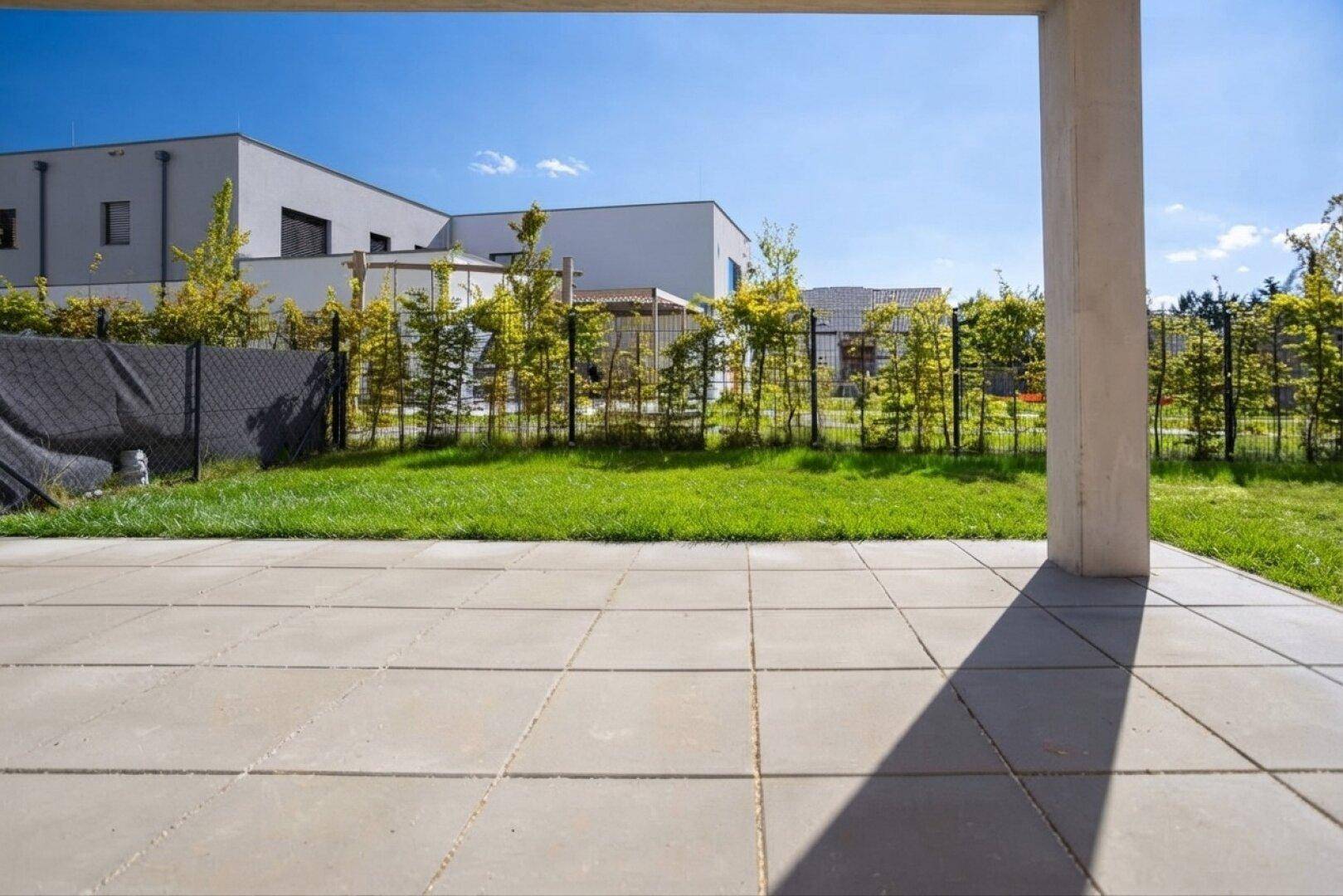 Geräumige, gepflasterte Terrasse mit Blick auf die grüne Umgebung und weitere Gebäude.