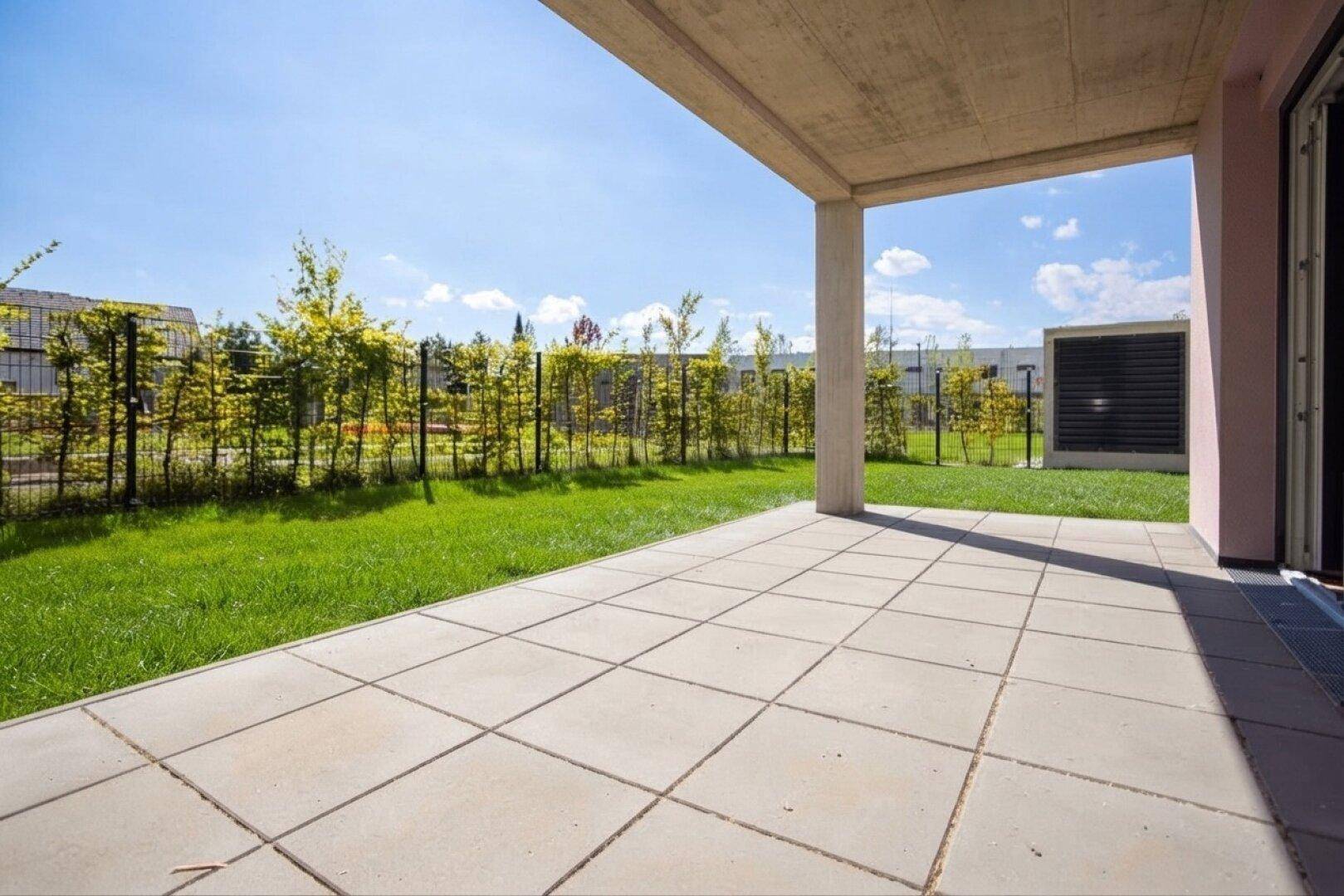 Sonnige Terrasse mit großformatigen Fliesen und Zugang zur privaten Rasenfläche.