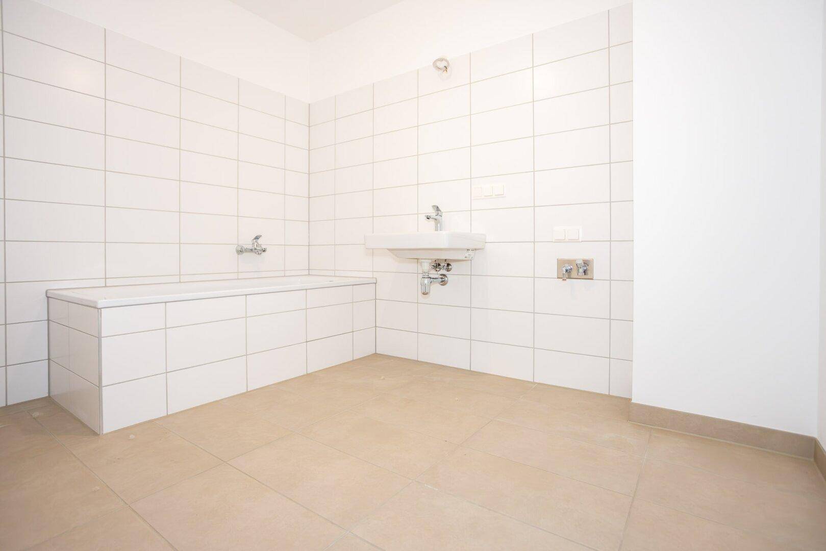Helles Badezimmer mit weißen Fliesen, Badewanne und Waschbecken, bereit für die Nutzung.