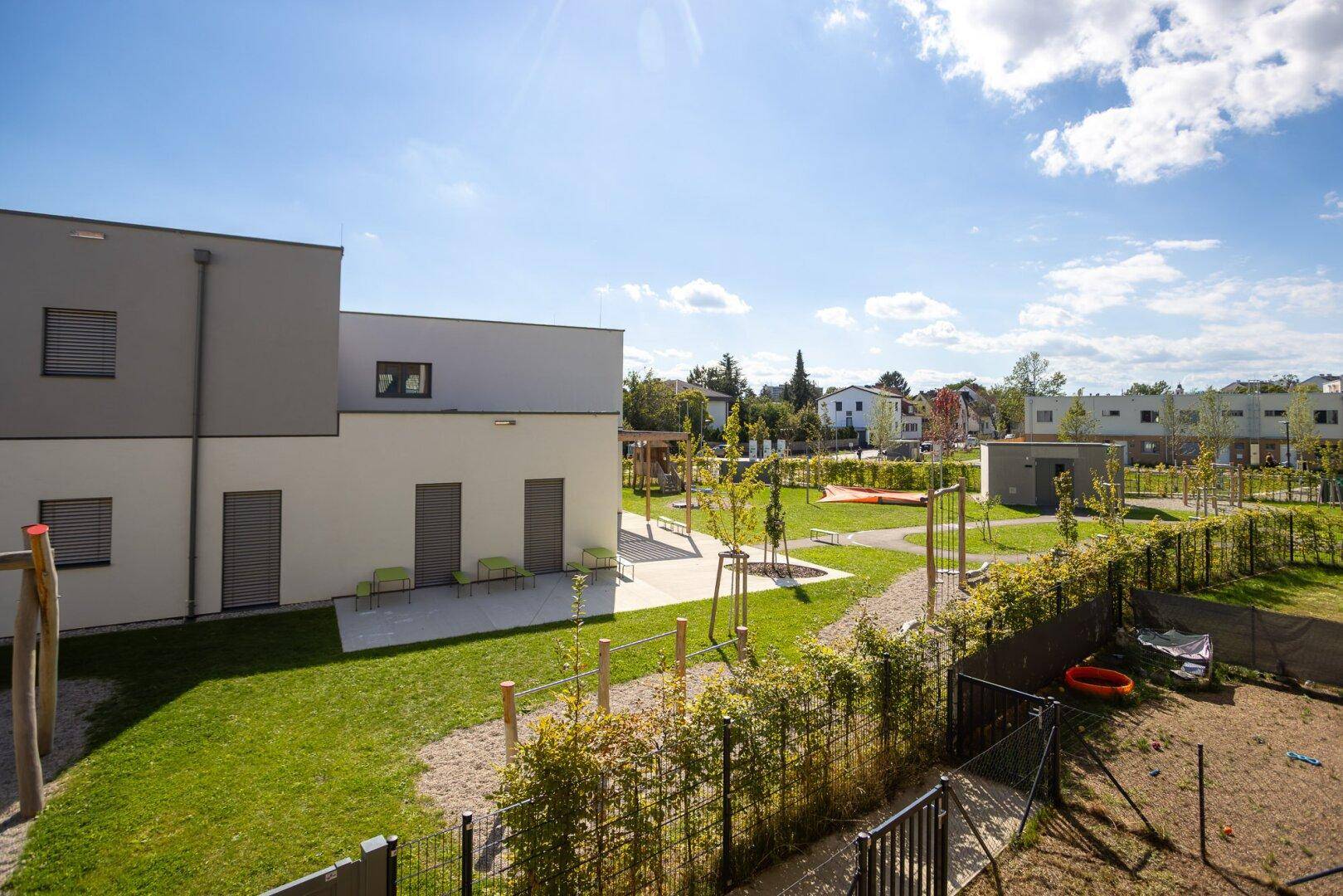 Weitläufige Grünflächen und ein Spielplatz innerhalb des modernen Wohnkomplexes unter blauem Himmel.