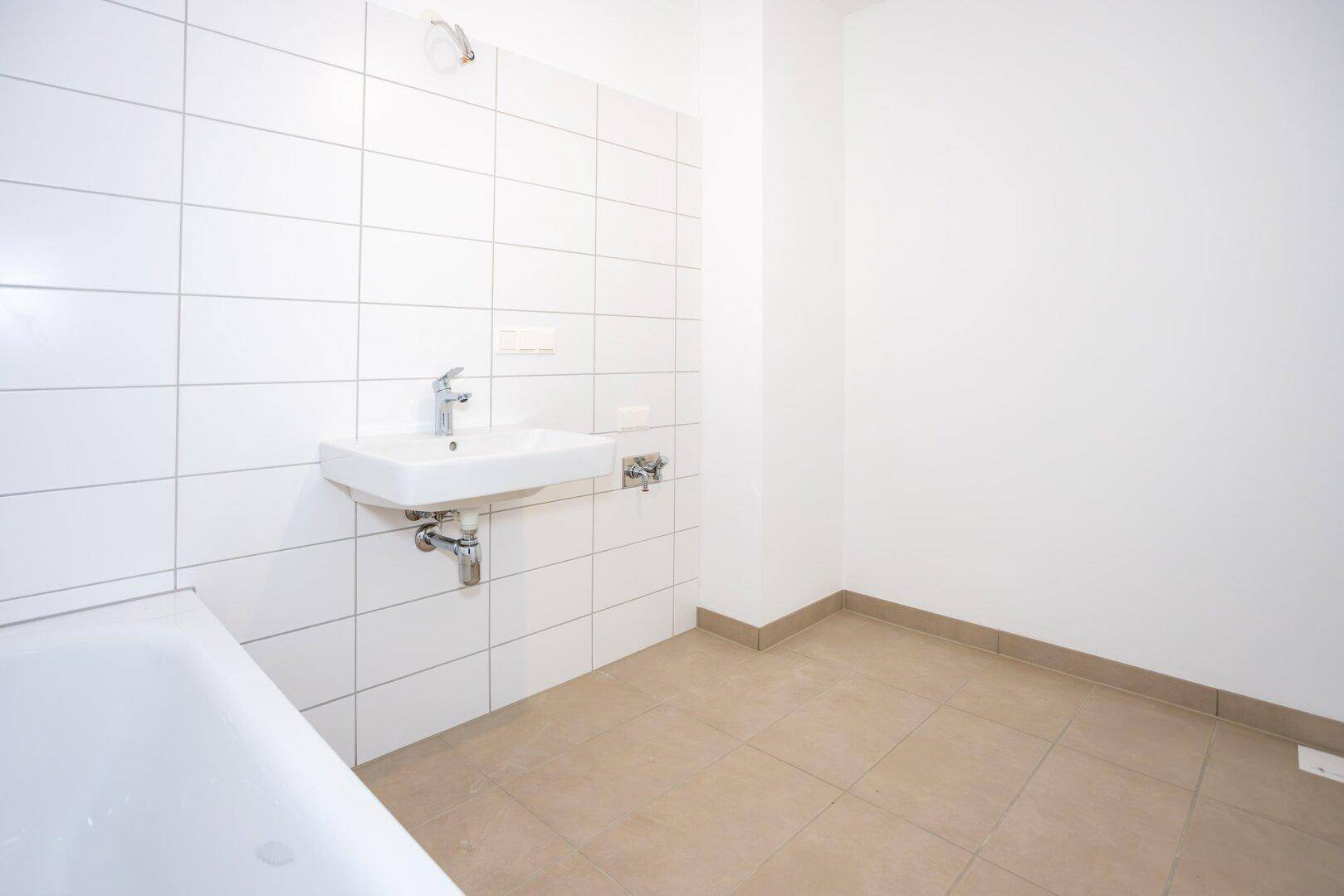 Funktionales Badezimmer mit weißen Wandfliesen, Waschbecken und Badewanne in neuwertigem Zustand.