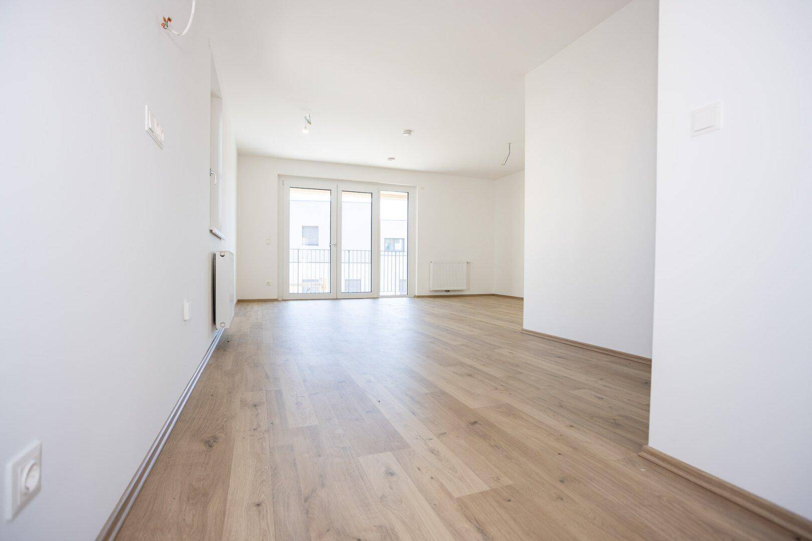 Geräumiges, unmöbliertes Zimmer mit Laminatboden und großen Fenstern, die viel Tageslicht hereinlassen.