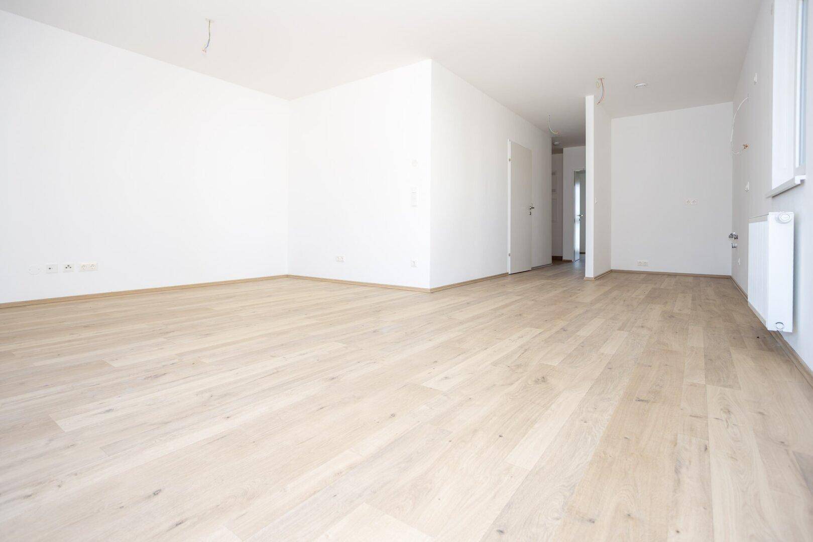 Heller Wohnbereich mit neuem Laminatboden und weißen Wänden, bereit für die individuelle Gestaltung.