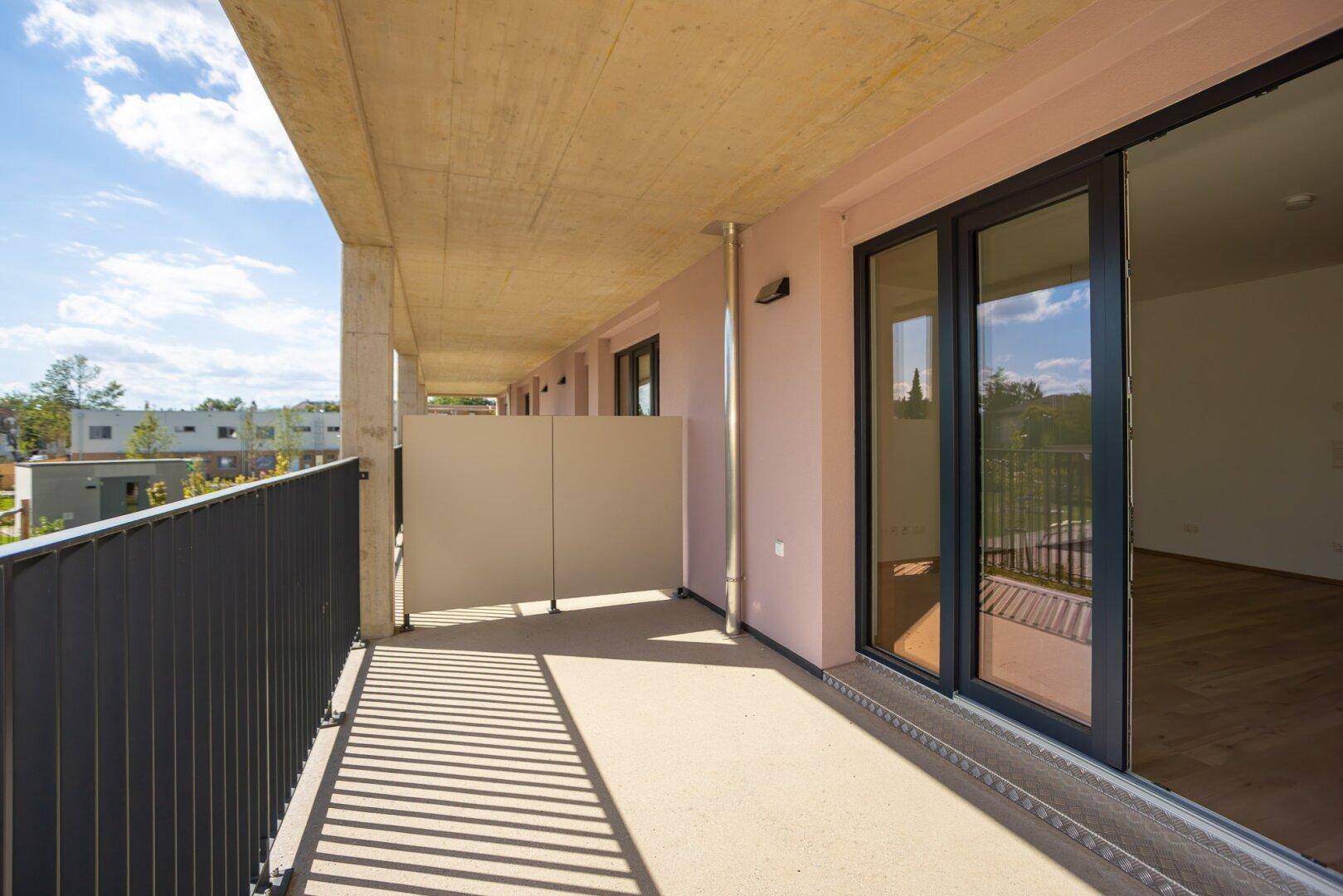 Langer Balkon mit Betonstruktur und Schiebetüren, die Zugang zu einem hellen Innenraum bieten.