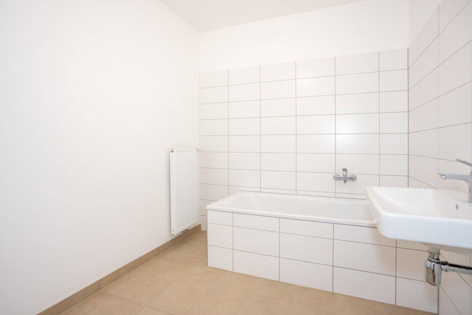 Modernes Badezimmer mit weißen Wandfliesen, Badewanne, Einzelwaschbecken und Heizkörper.