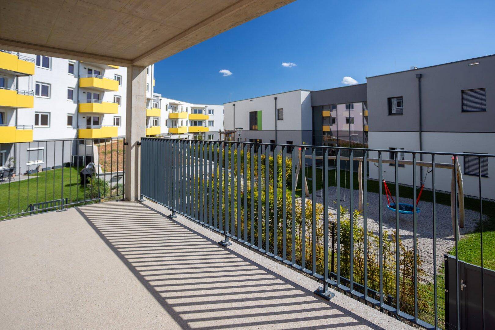 Geräumiger Balkon mit Blick auf den gemeinschaftlichen Spielplatz und die modernen Wohngebäude.