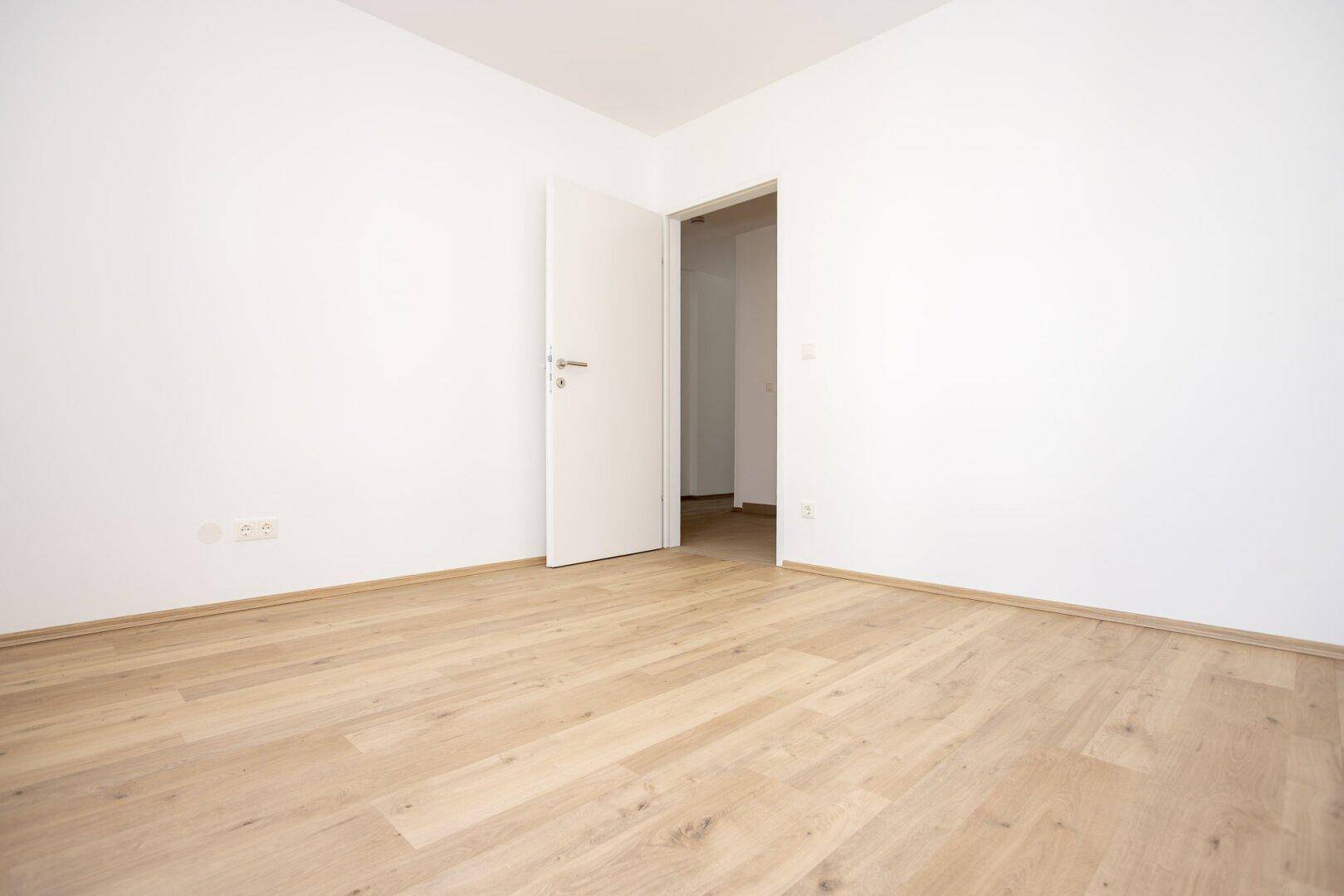 Leeres Schlafzimmer mit Laminatboden und weiß gestrichenen Wänden, bereit zur Einrichtung.