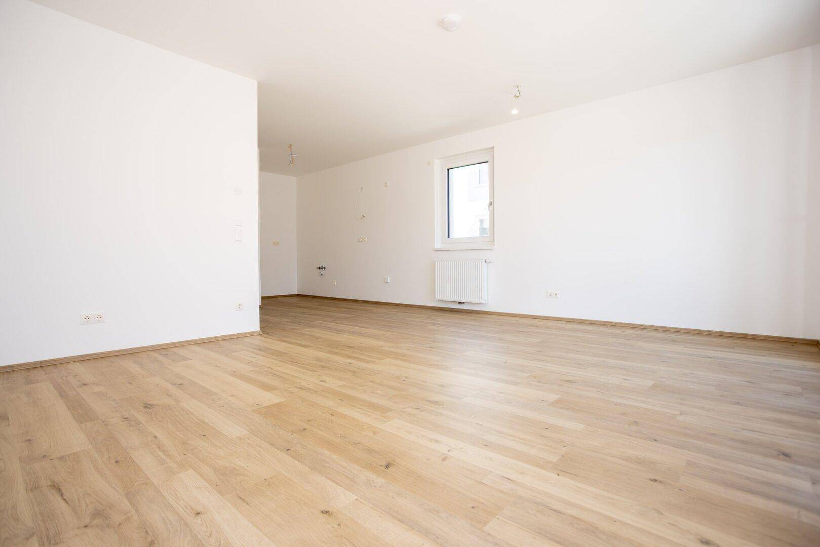 Lichtdurchflutetes Zimmer mit hellem Laminatboden und weißen Wänden, ideal für ein Wohn- oder Schlafzimmer.