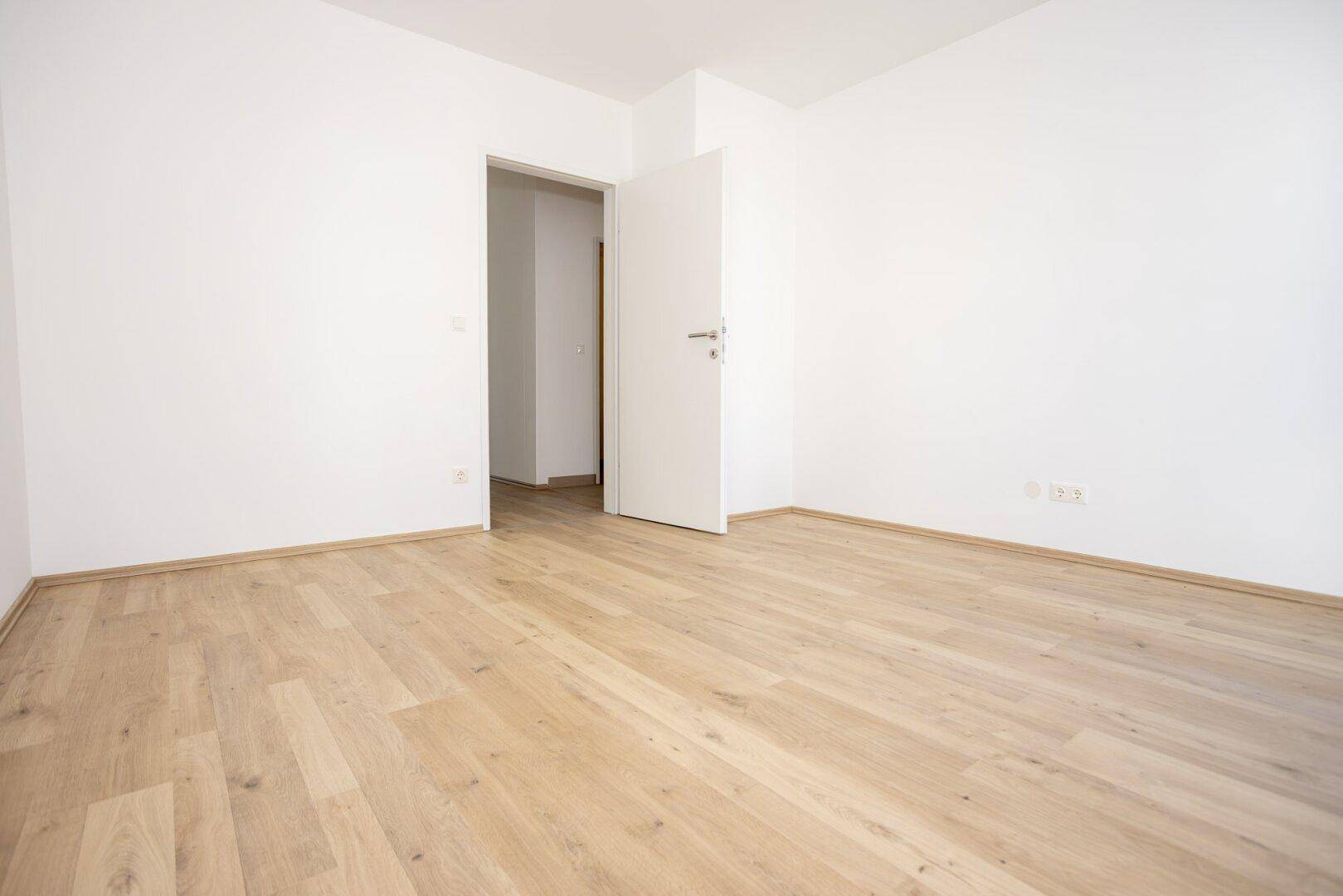 Unmöbliertes Zimmer mit Laminatboden und weißen Wänden, das vielseitig genutzt werden kann.