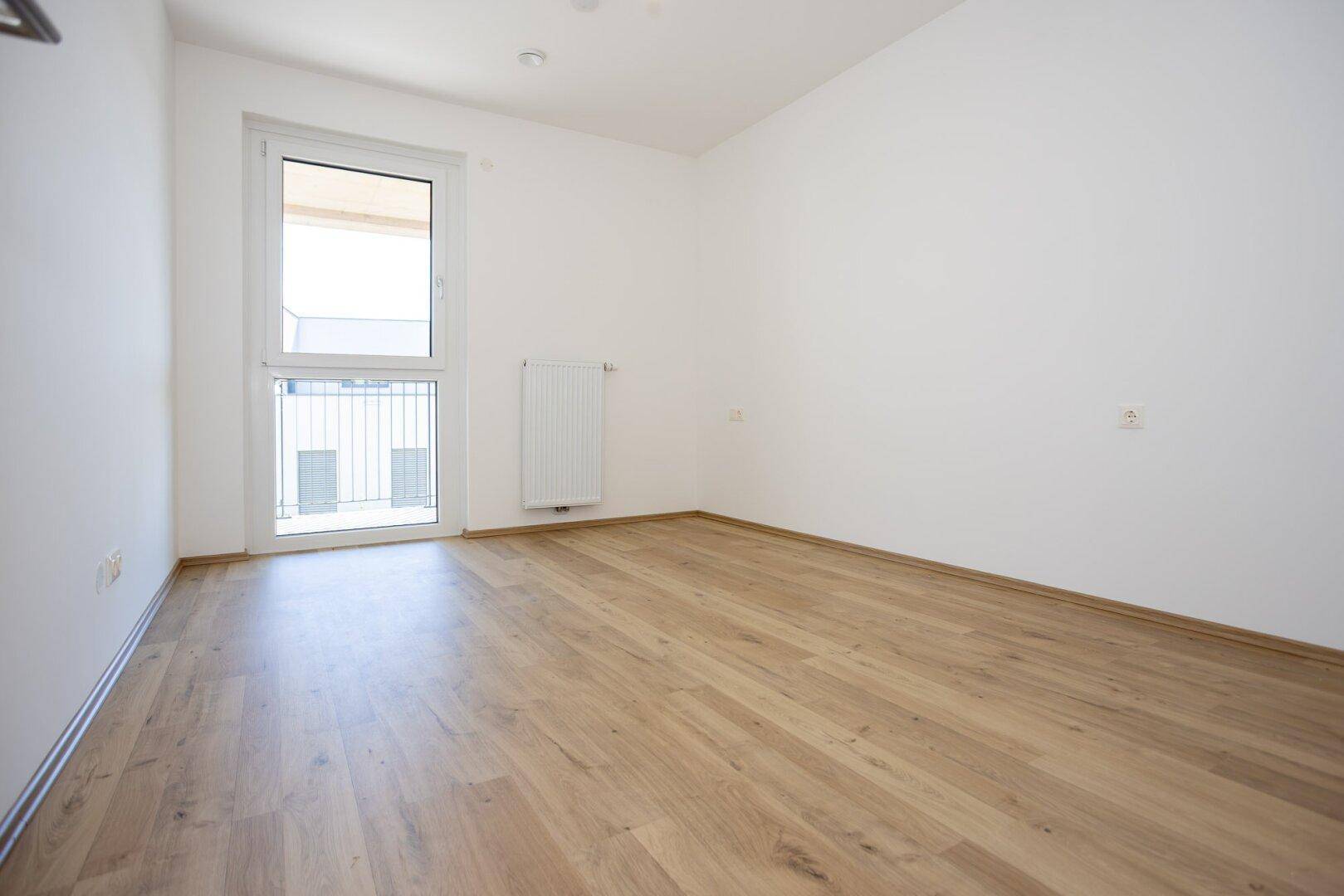 Kleineres Zimmer mit Holzboden und Fenster, das viel Tageslicht hereinlässt.