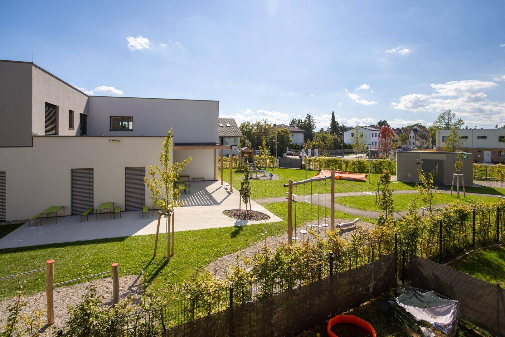 Grüne Außenanlage mit Spielplatz und modernen Wohngebäuden im Hintergrund.
