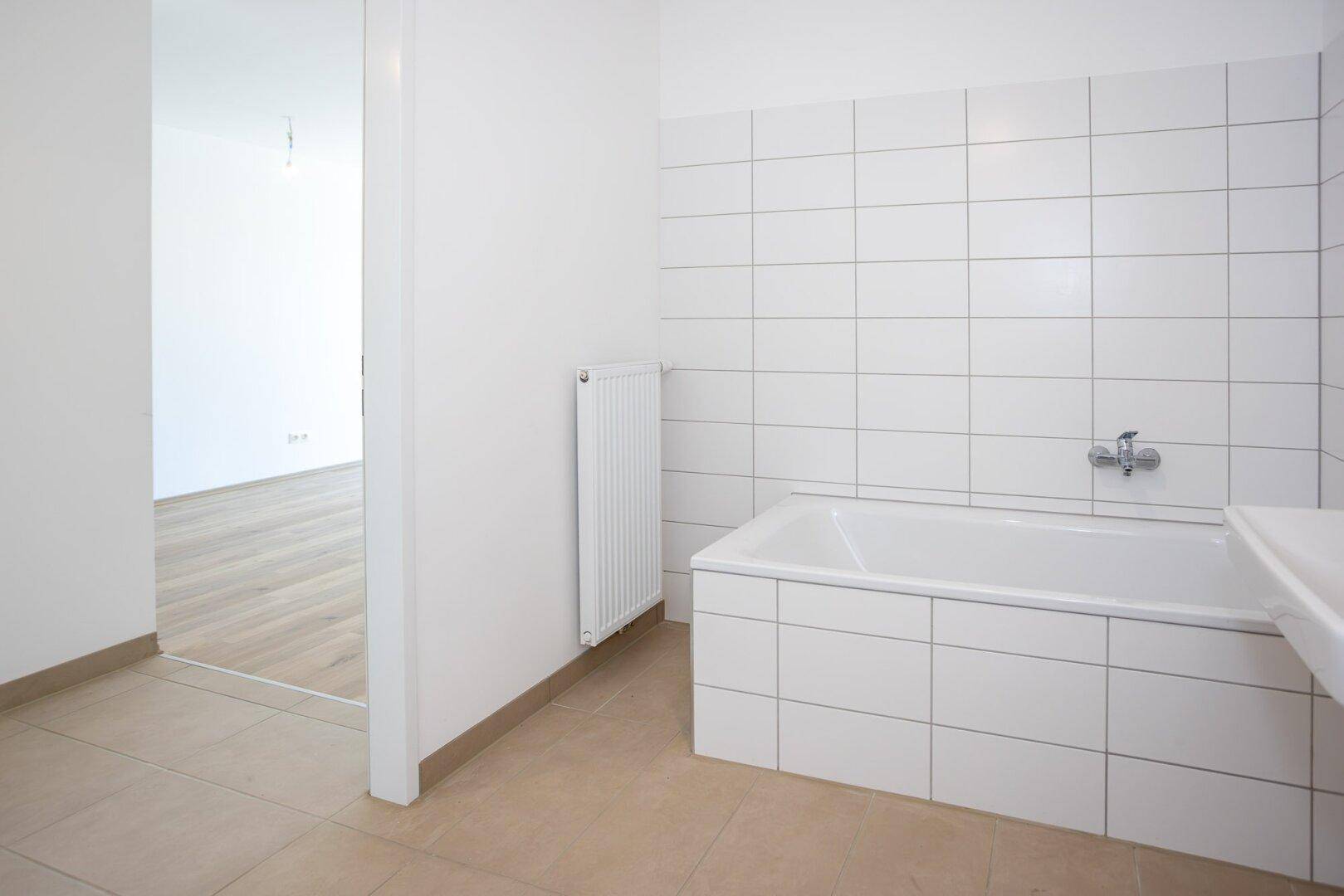 Badezimmer mit weiß gefliesten Wänden, Badewanne und beigefarbenem Fliesenboden.