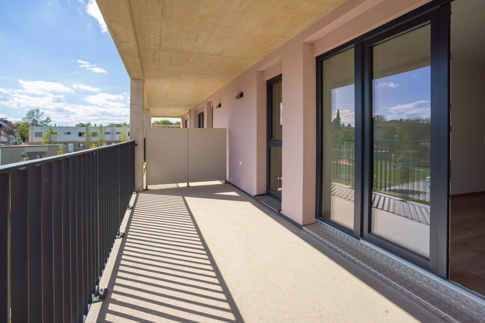 Breiter Balkon mit Schiebetüren und Blick auf die grüne Umgebung und weitere Gebäude.