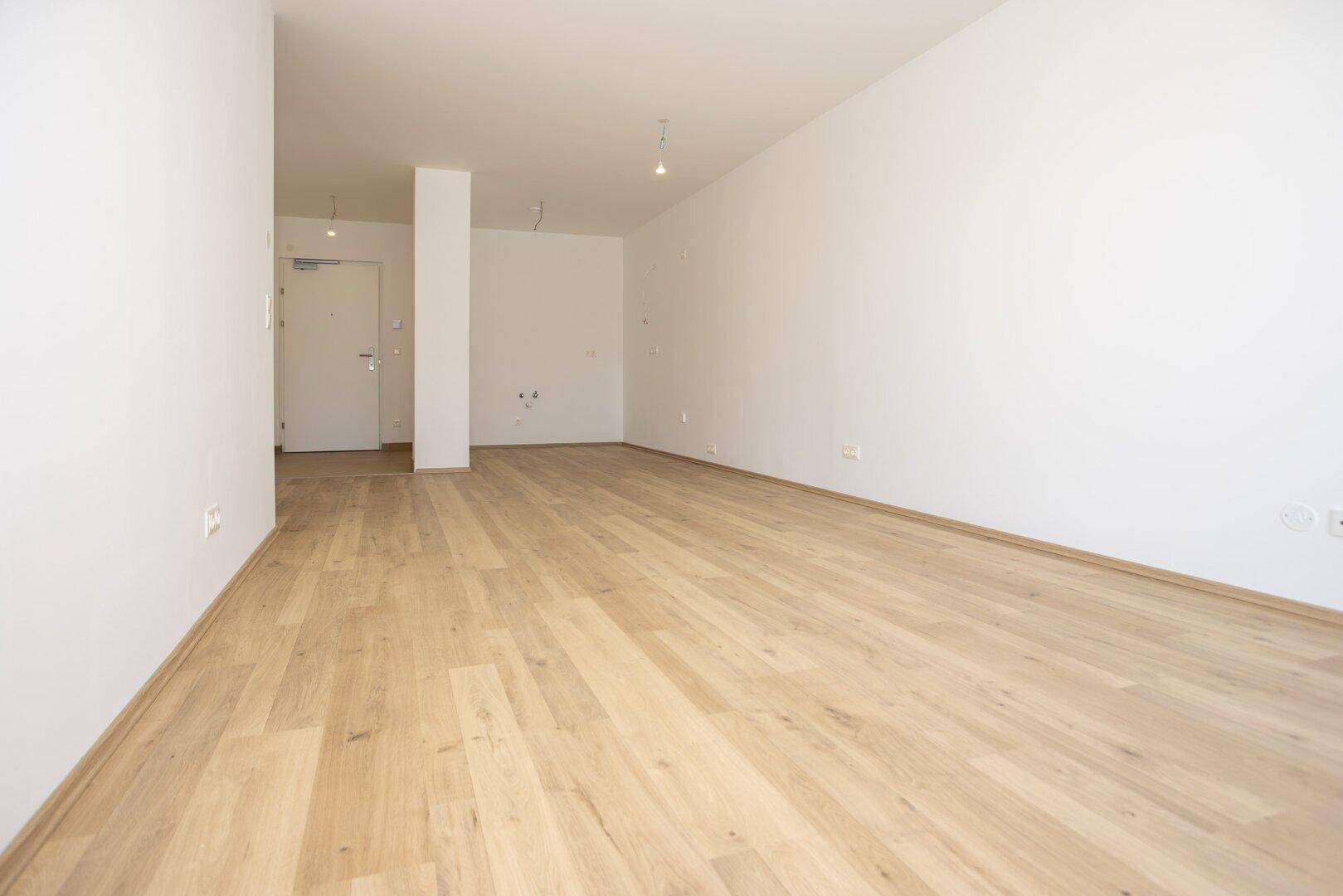 Geräumiger, leerer Raum mit Holzboden und weiß gestrichenen Wänden, bereit zum Einzug.