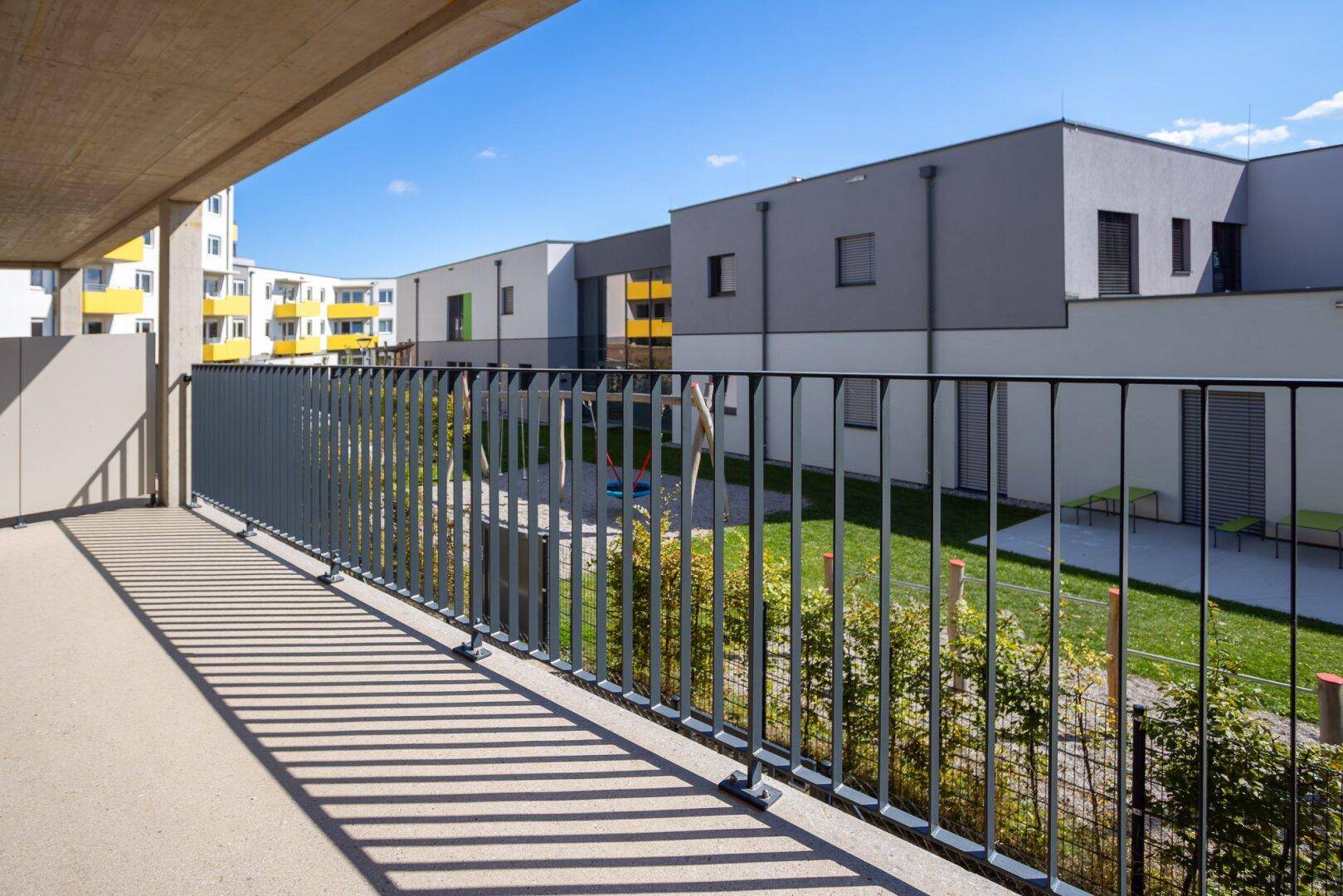 Balkon mit Blick auf einen modernen Spielplatz und die umliegenden Neubauten.