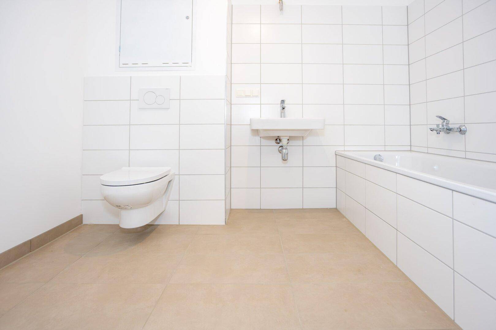 Modernes Badezimmer mit weißen Fliesen, wandhängendem WC, Waschbecken und Badewanne.