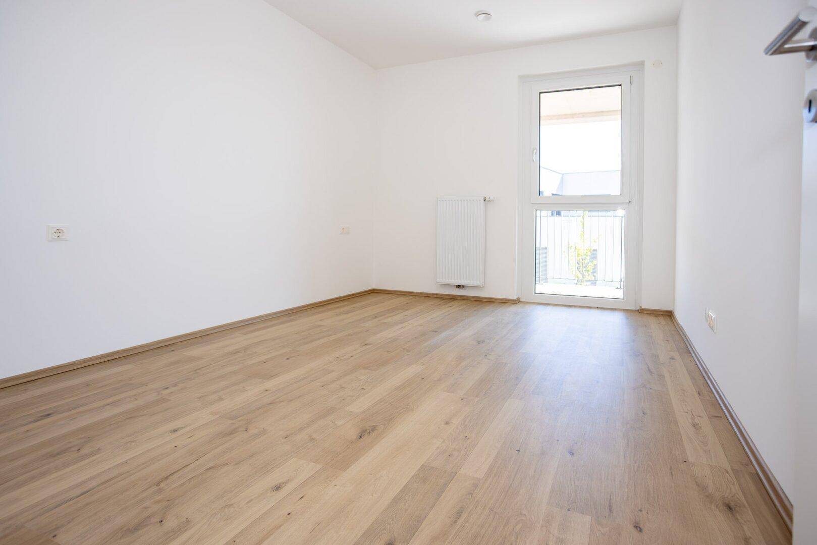 Helles Schlafzimmer mit Laminatboden und Zugang zu einem französischen Balkon.