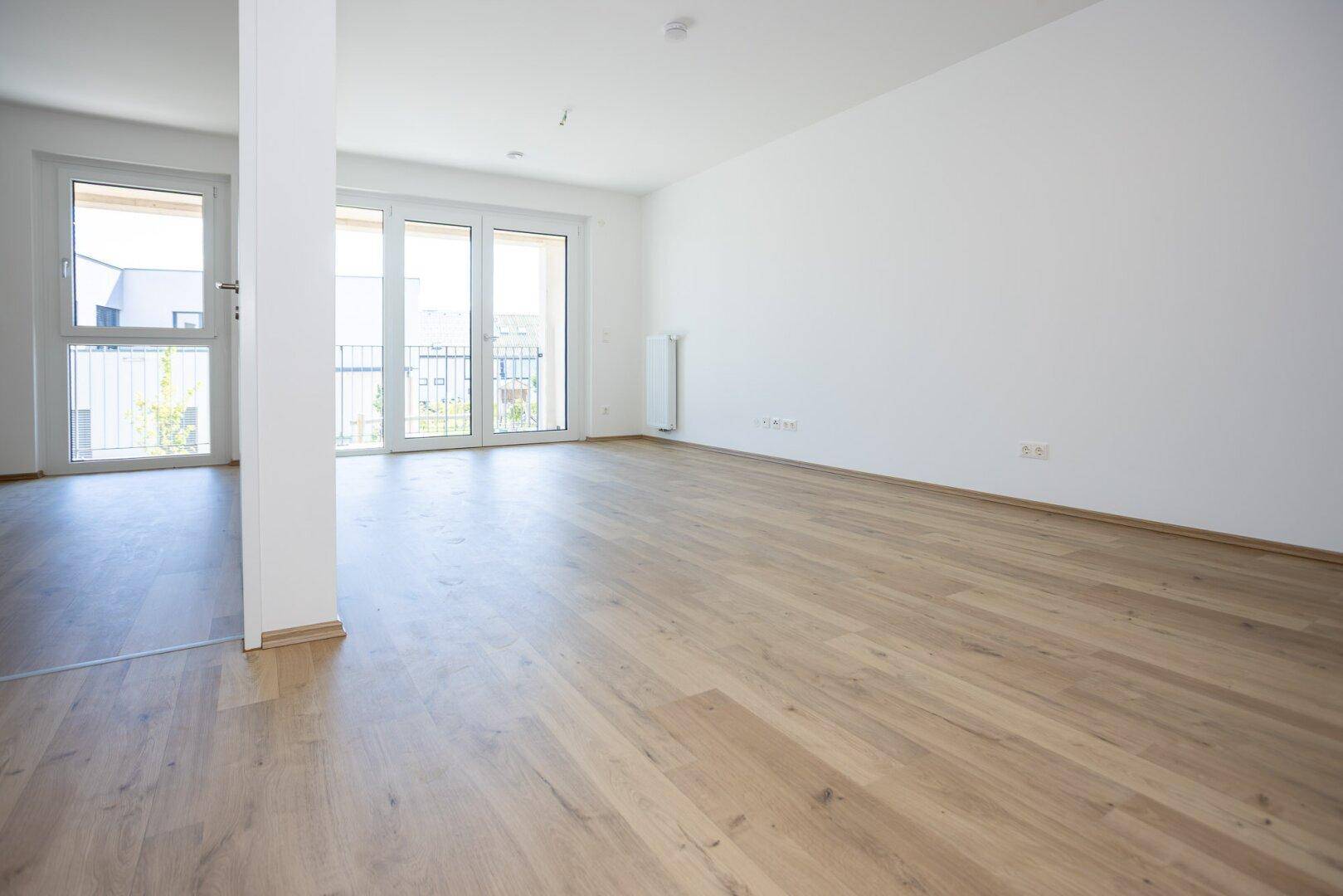 Geräumiges Wohnzimmer mit hellem Laminatboden und großen Fenstern für viel Tageslicht.
