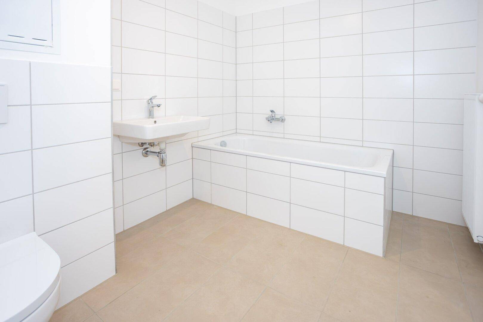 Helles Badezimmer mit Badewanne, Waschbecken und weißen Wandfliesen.