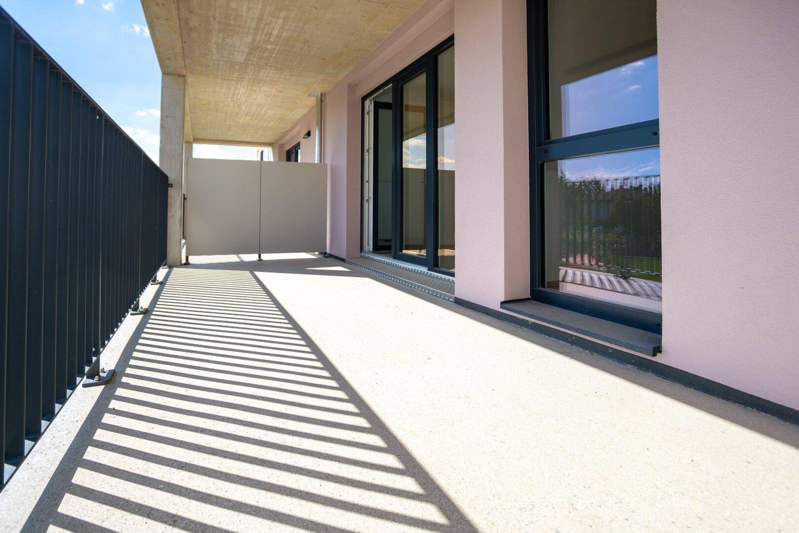 Sonniger Balkon mit großen Glasfenstern und Blick auf die umliegende Bebauung.