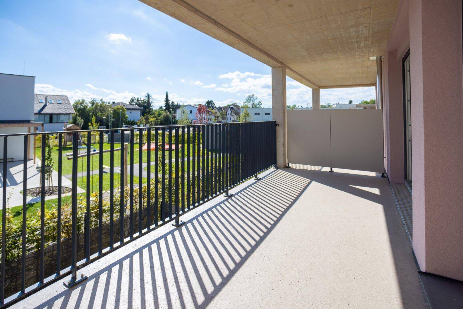 Heller Balkon mit Betonboden und Blick auf die Umgebung und den grünen Innenhof.