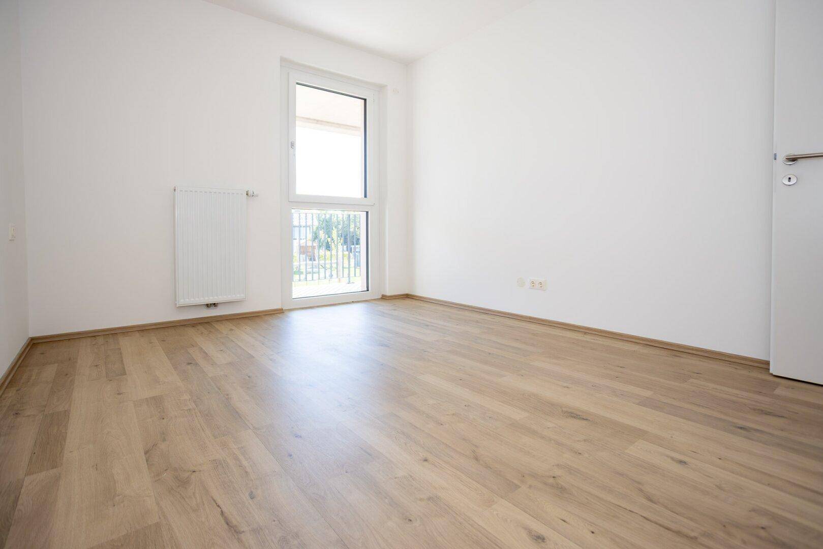 Geräumiges Schlafzimmer mit hellem Laminatboden und Fenster für viel Tageslicht.